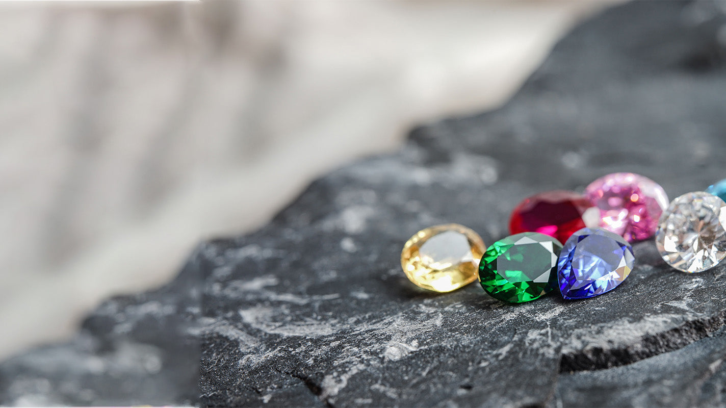 Vibrant gemstones in yellow, green, blue, pink, and red rest on a dark, textured rock surface.