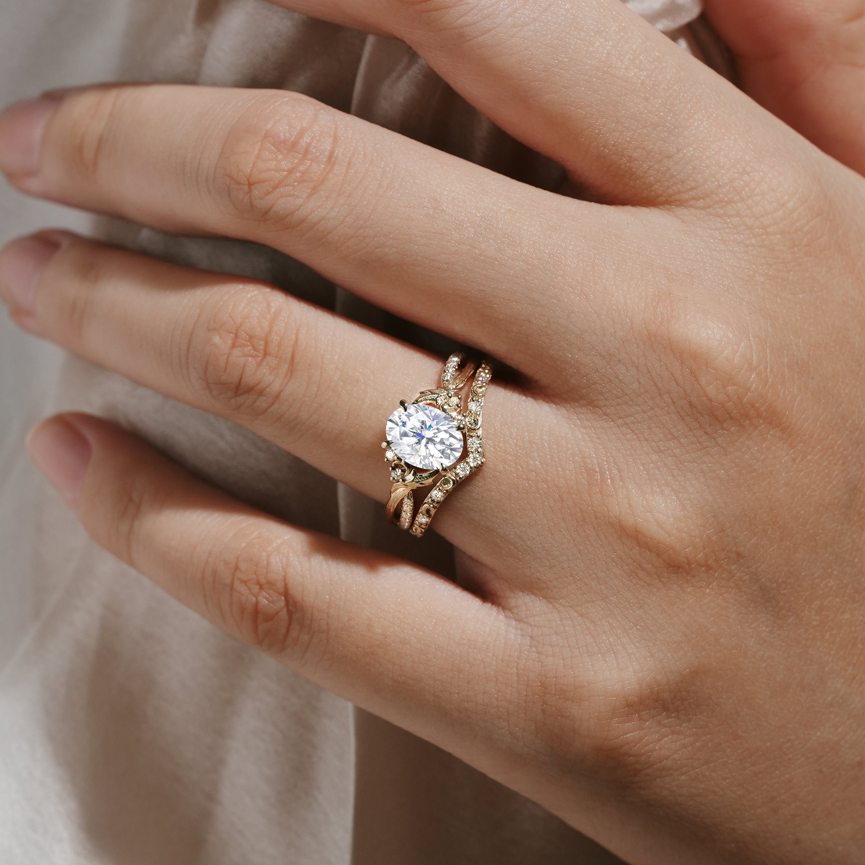 Moissanite leaf engagement ring set with a bark texture and V-shaped wedding band, on a hand.