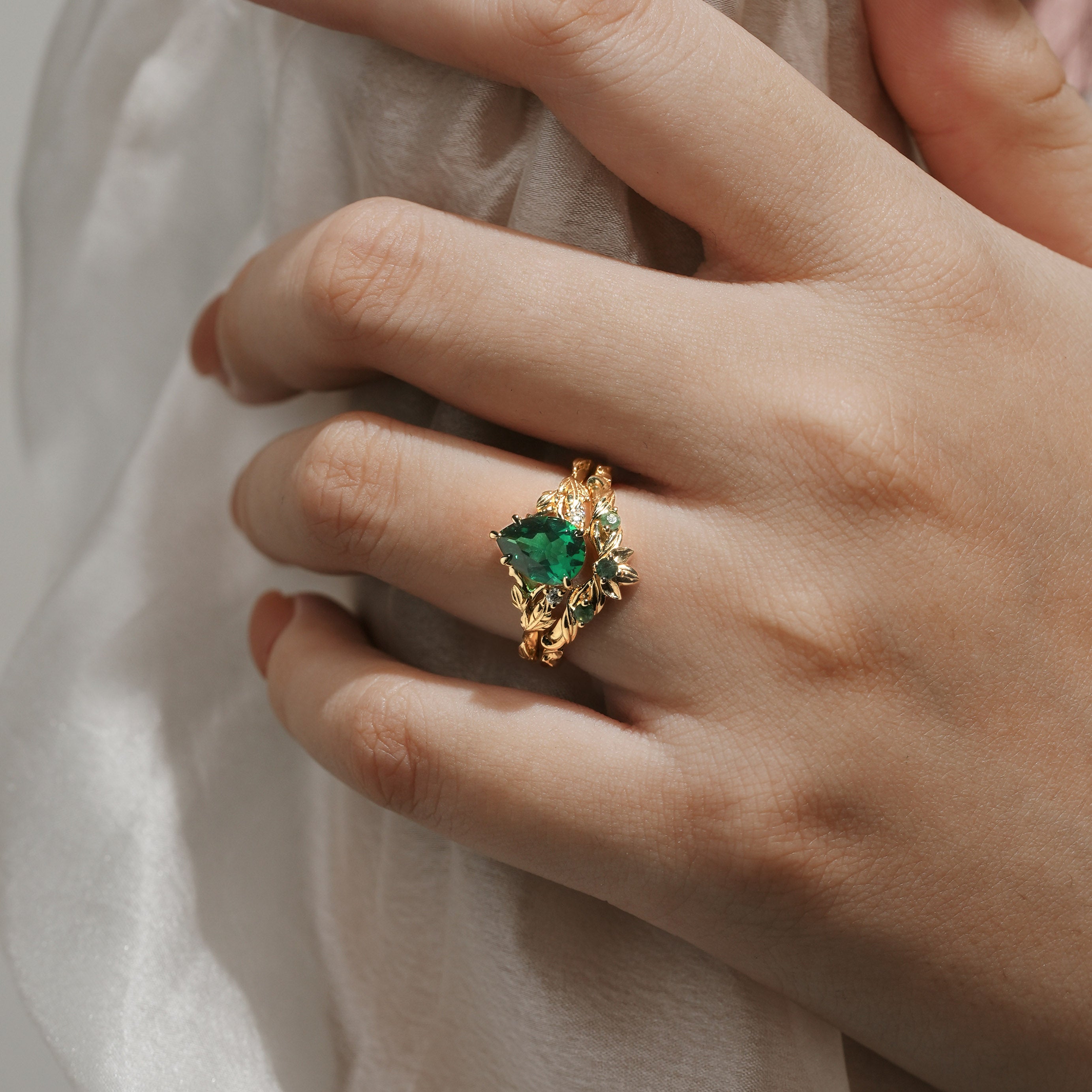 Woman's hand wearing a gold pear-cut emerald leaf bridal set; wedding and engagement ring