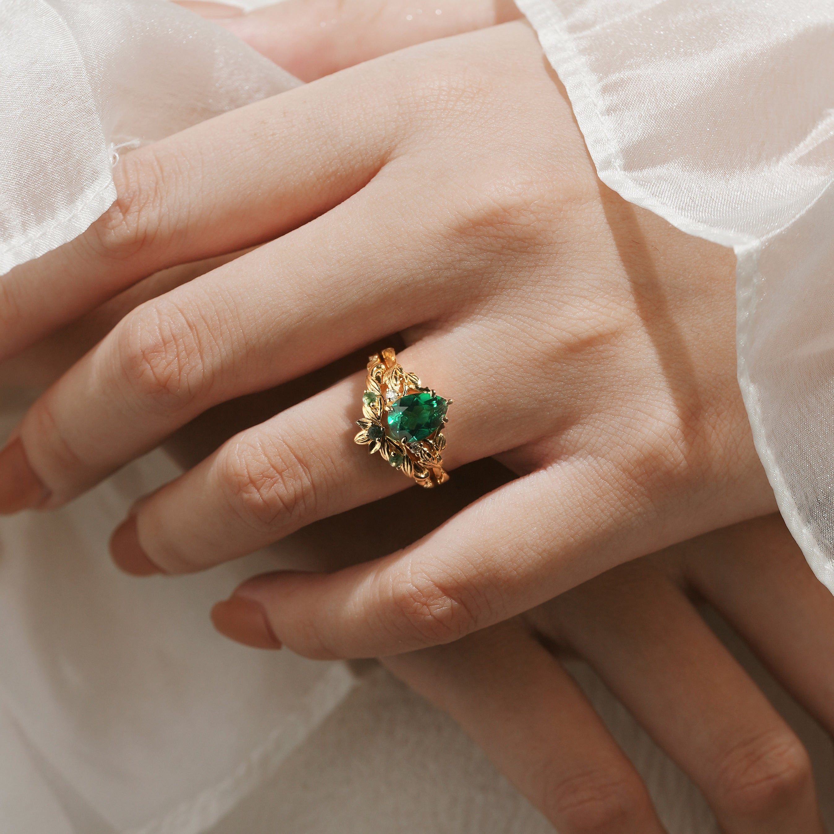Woman's hand wearing a solid gold pear cut emerald leaf engagement ring. Vintage bridal set.