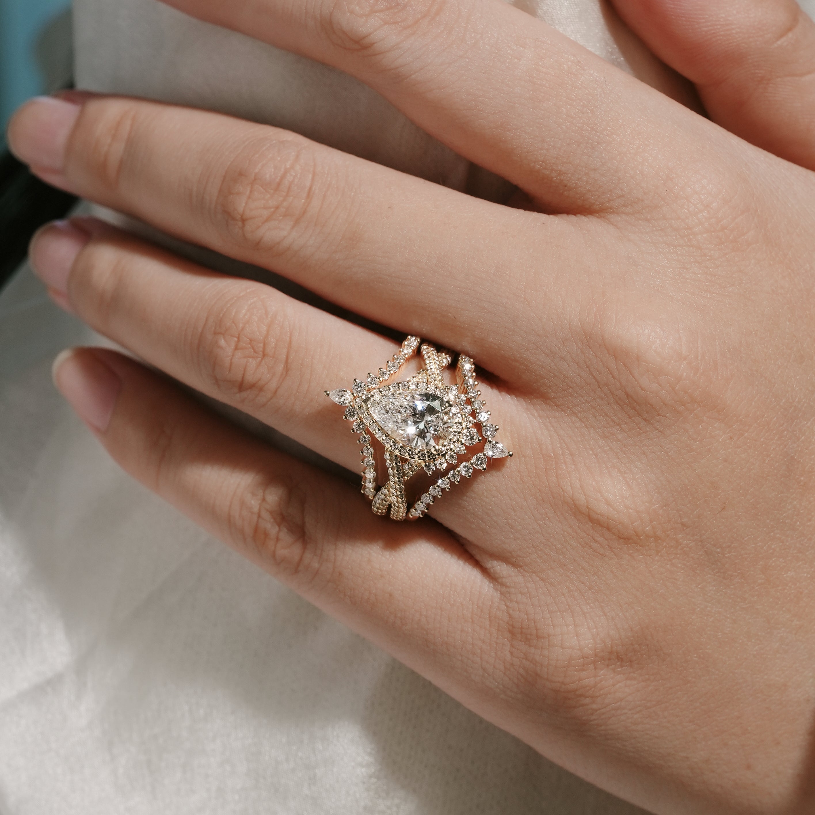 Woman's hand wearing pear cut halo moissanite engagement ring set, Lahela Jewelry