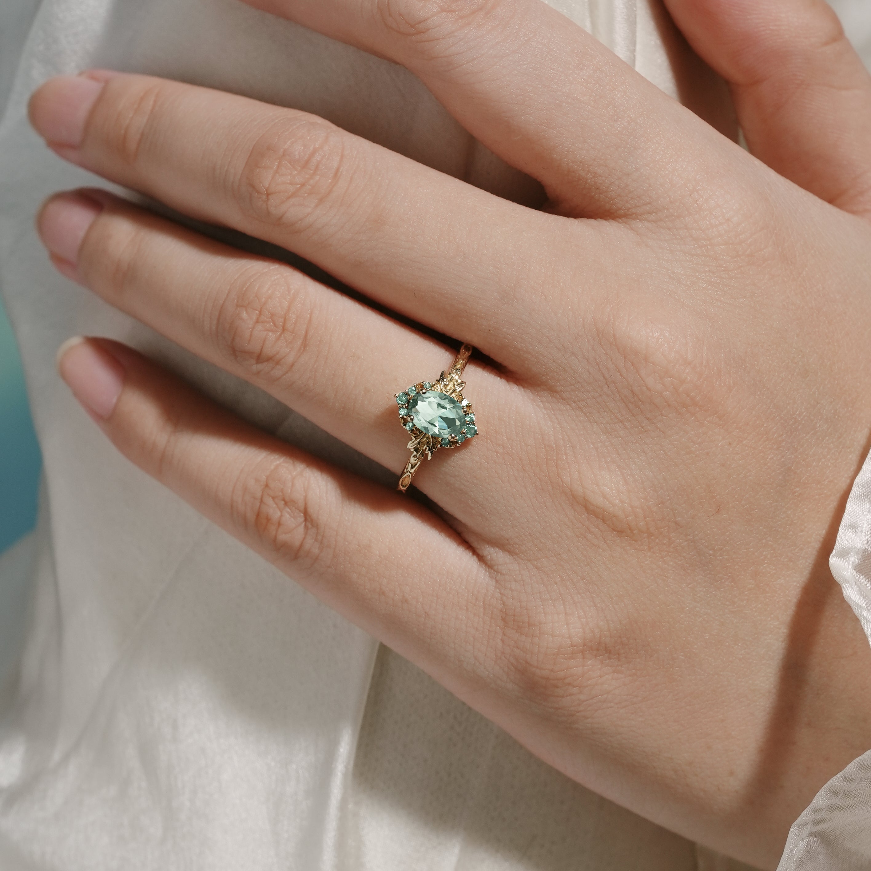 Oval green sapphire engagement ring with leaf design on a hand, gold band, bridal set