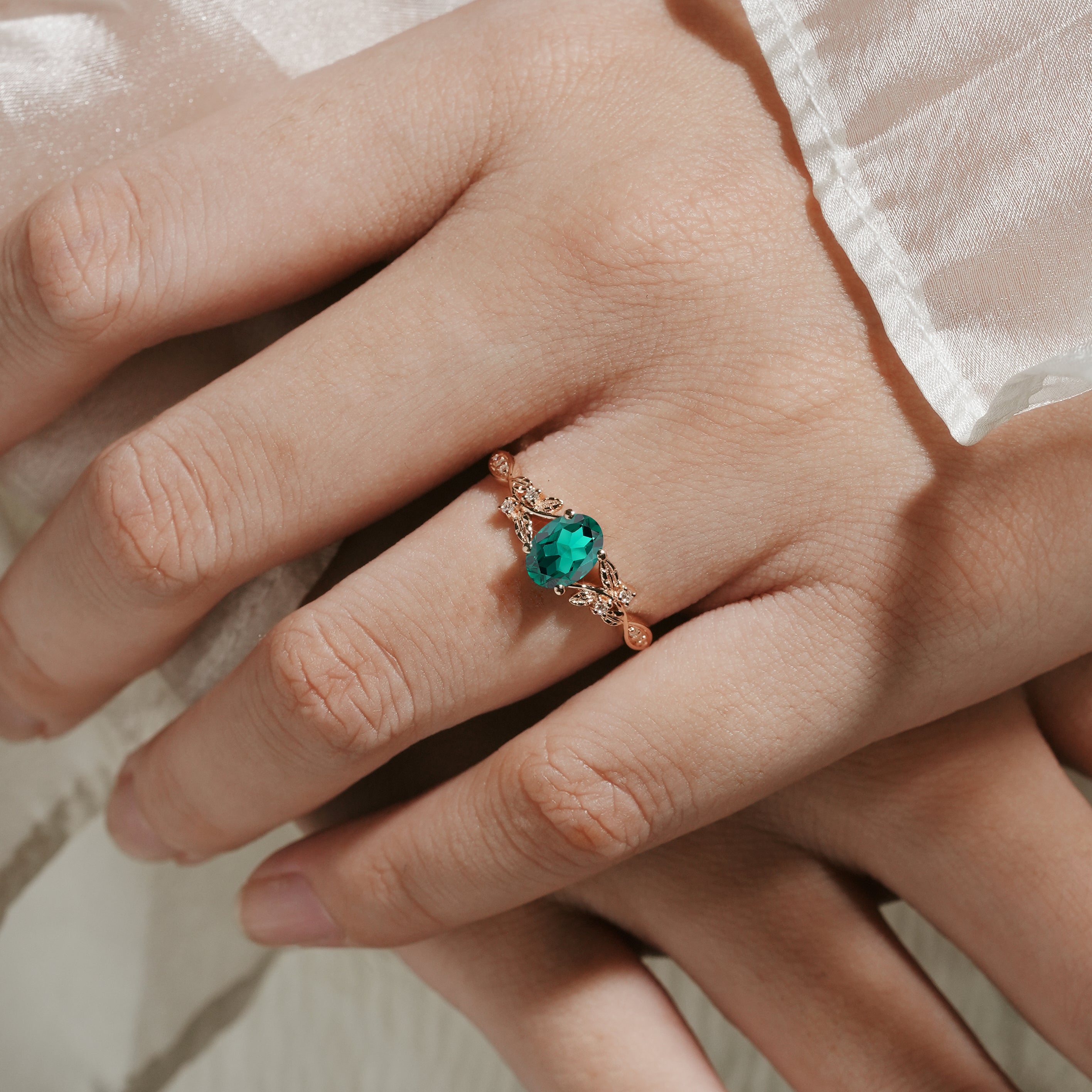Rose gold oval lab grown emerald engagement ring with leaf design on a hand. Vintage-style wedding ring.