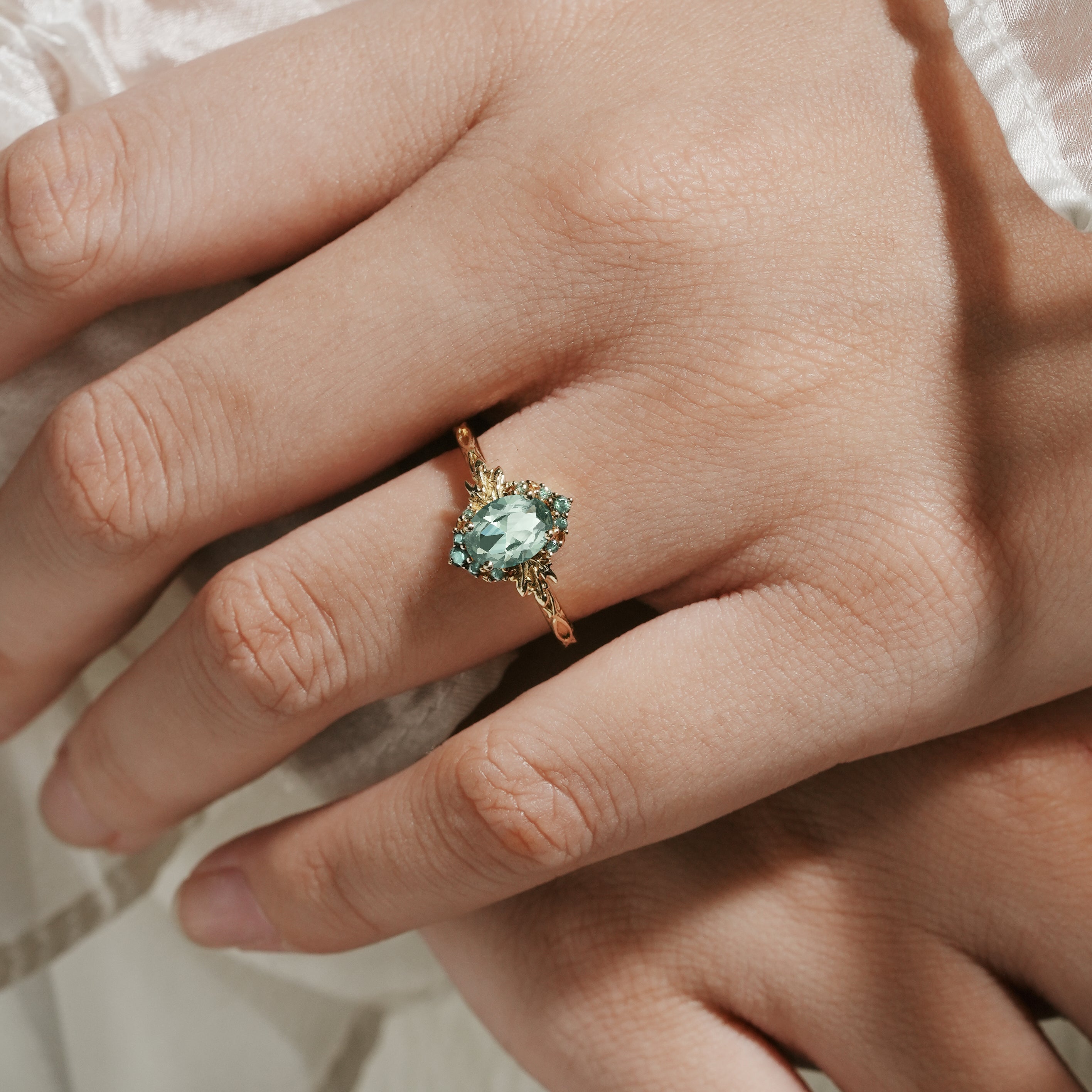 Oval green sapphire engagement ring with leaf design on hand, bridal jewelry.