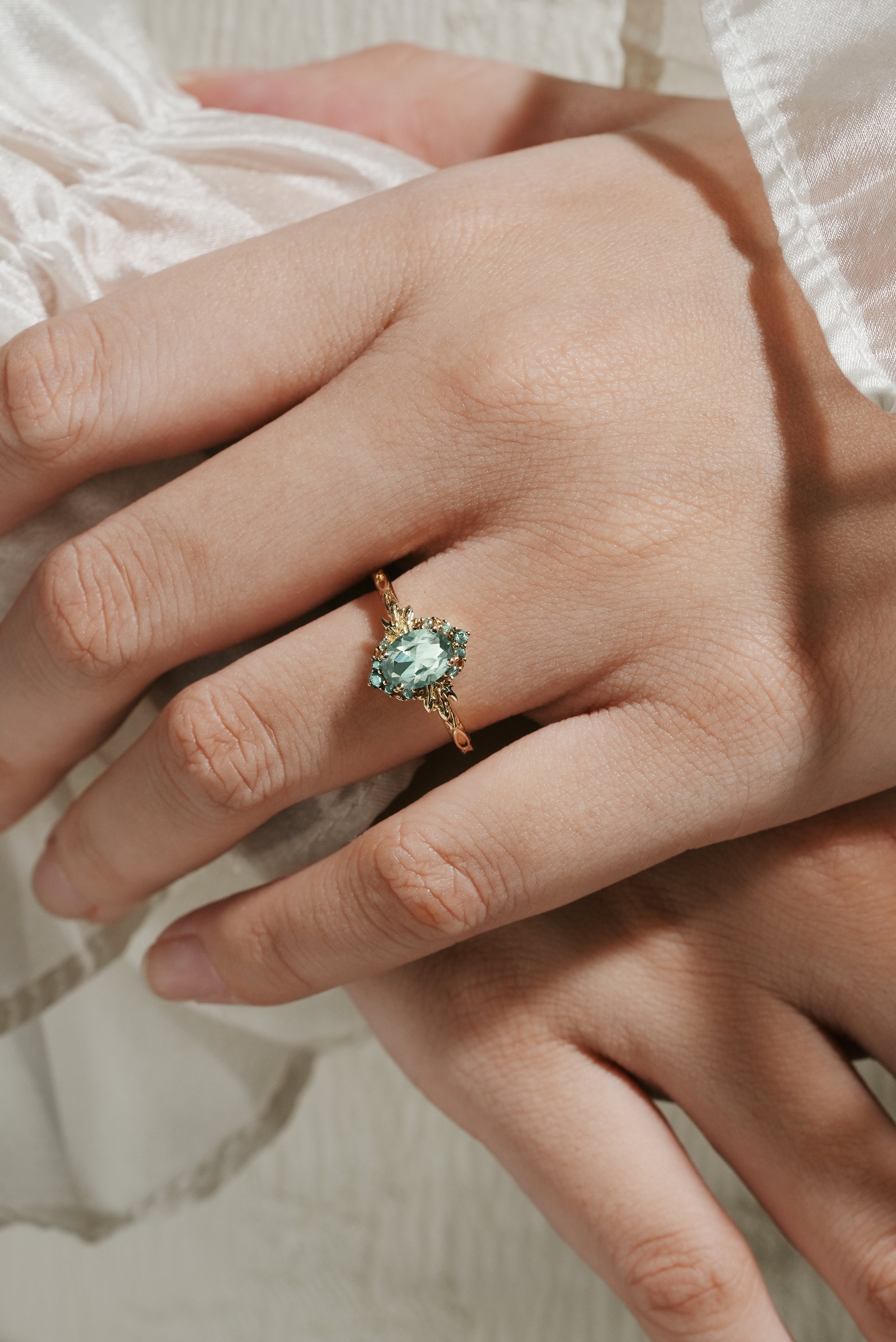 Oval green sapphire engagement ring with leaf design on hand, bridal jewelry.