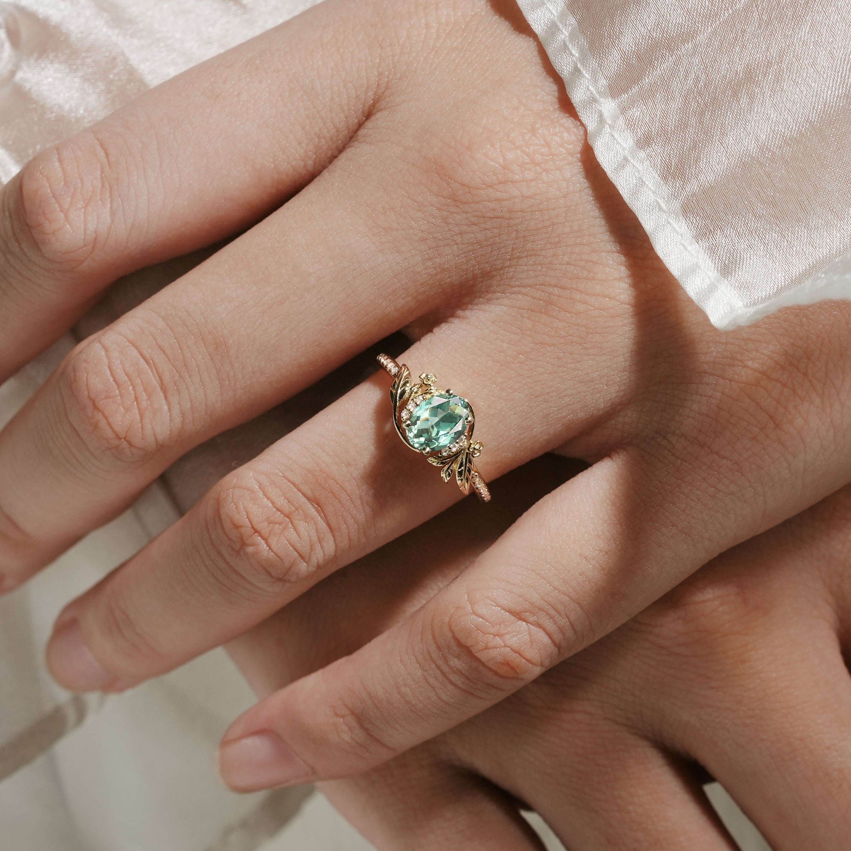 Oval green sapphire engagement ring with leaf and flower accents on a hand, Lahela Jewelry