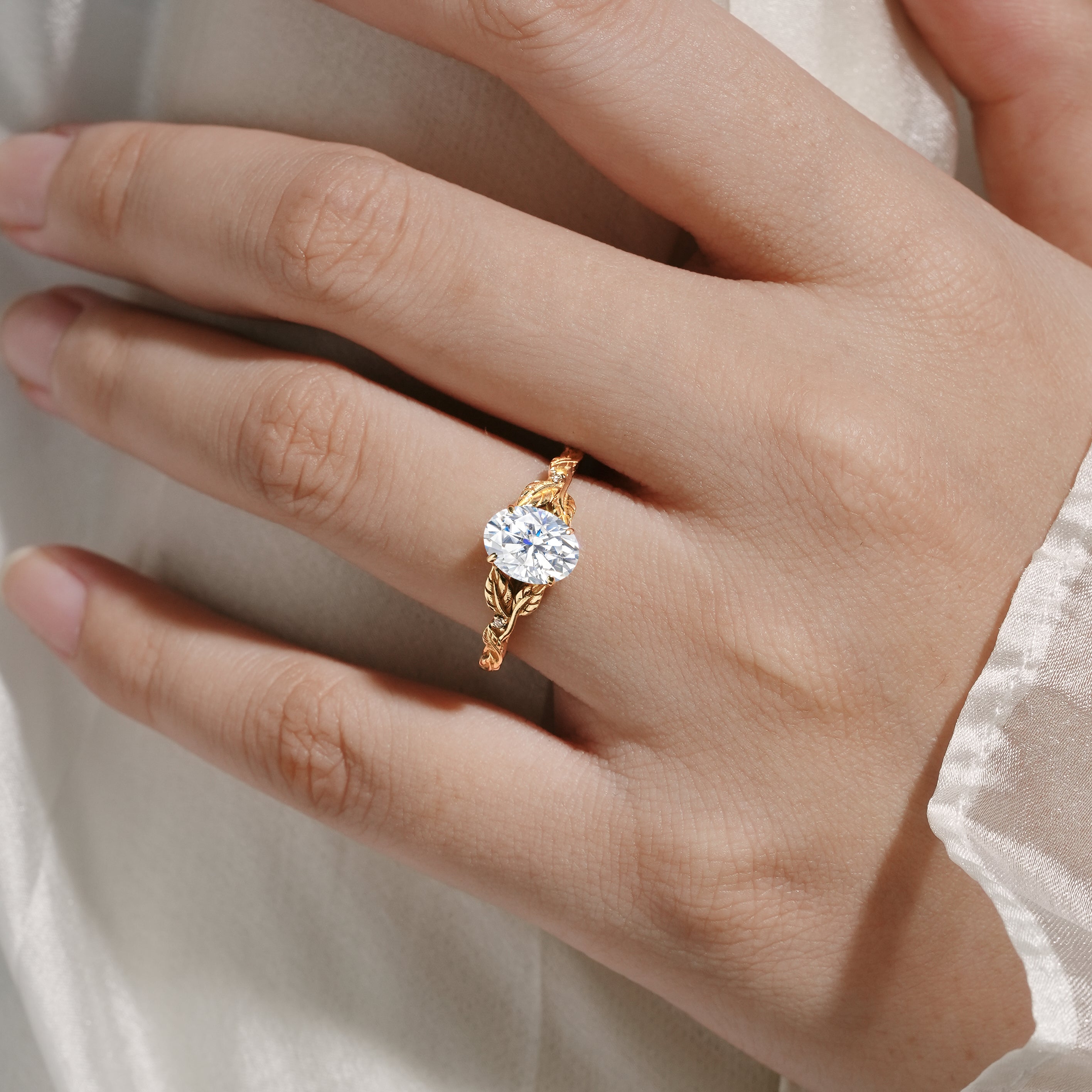 Oval moissanite engagement ring with leaf-inspired band on hand. 14k gold, bridal ring.