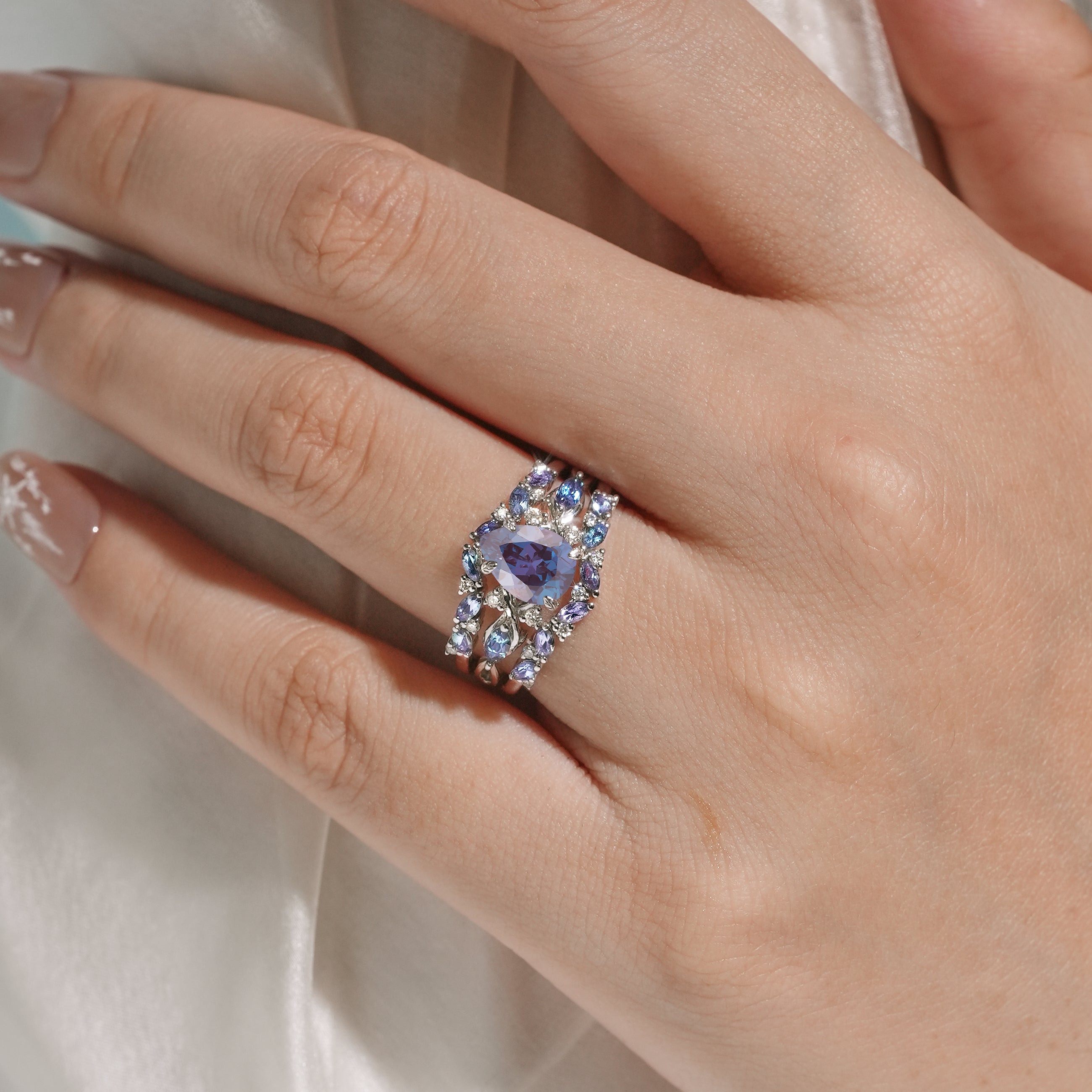 Alexandrite ring set on finger, showing pear cut gemstone and enhancer band