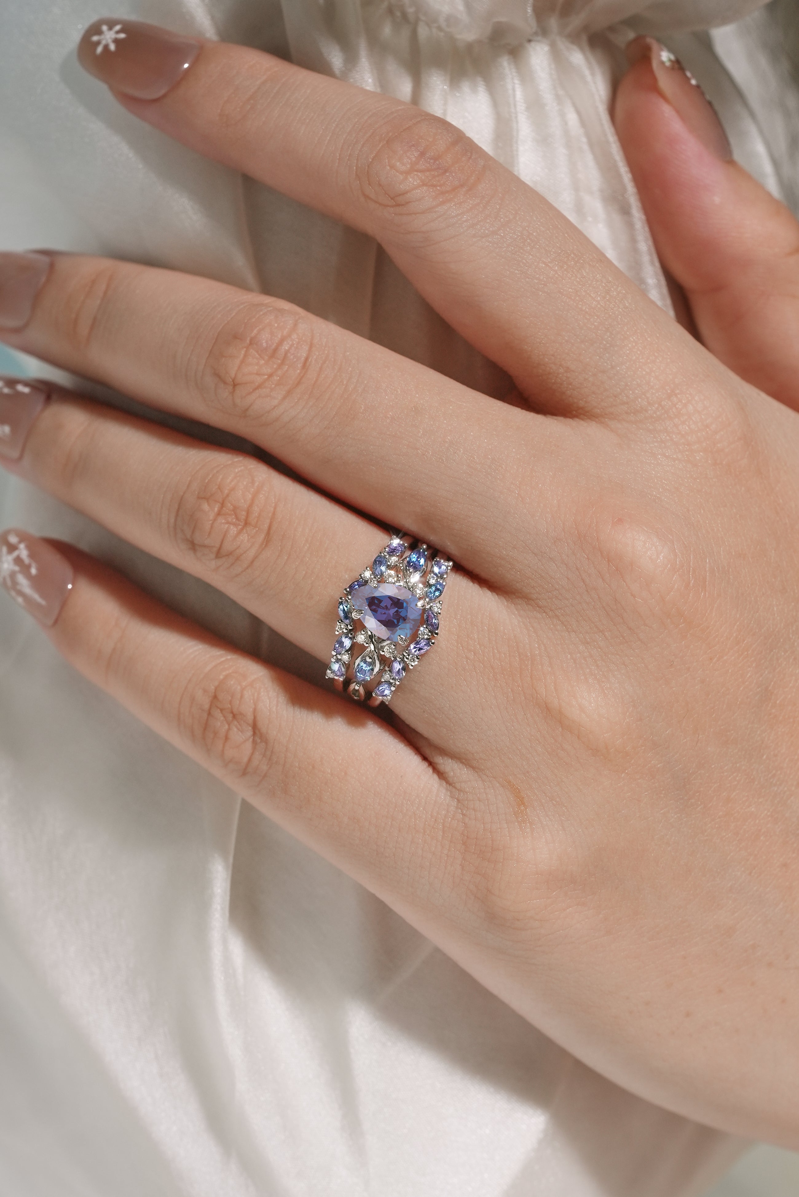 Alexandrite ring set on finger, showing pear cut gemstone and enhancer band