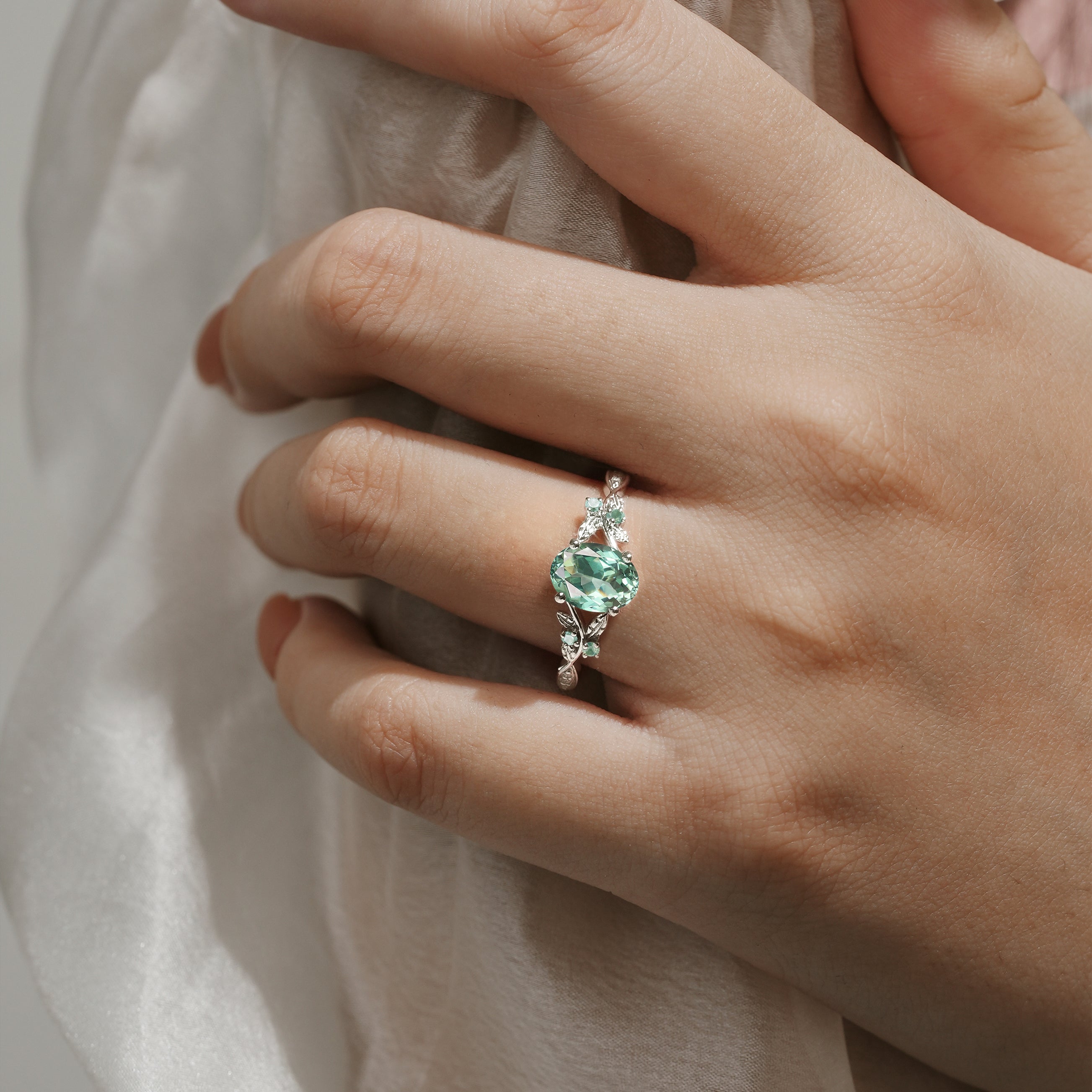 Oval green sapphire engagement ring on hand with leaf details
