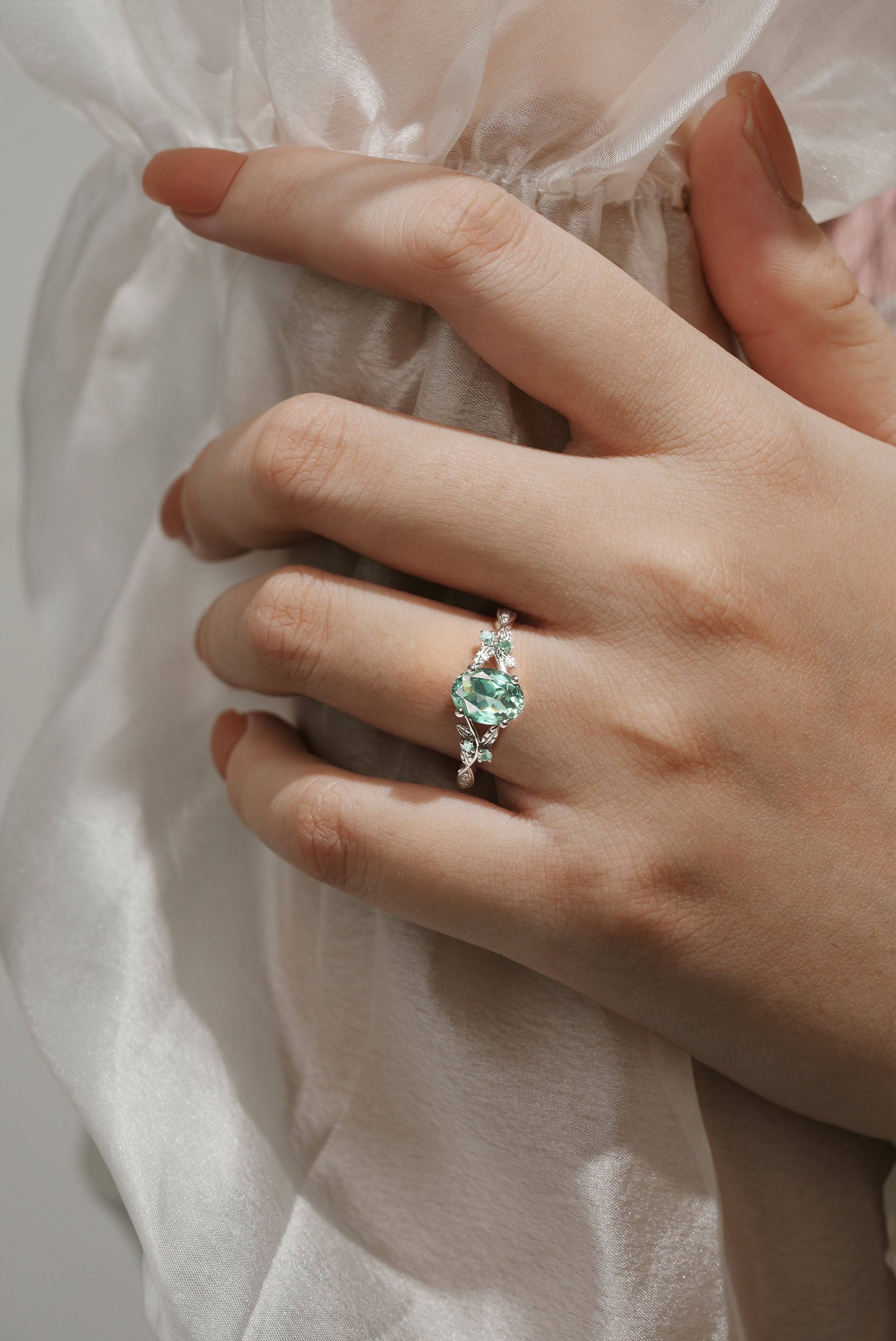 Oval green sapphire engagement ring on hand with leaf details