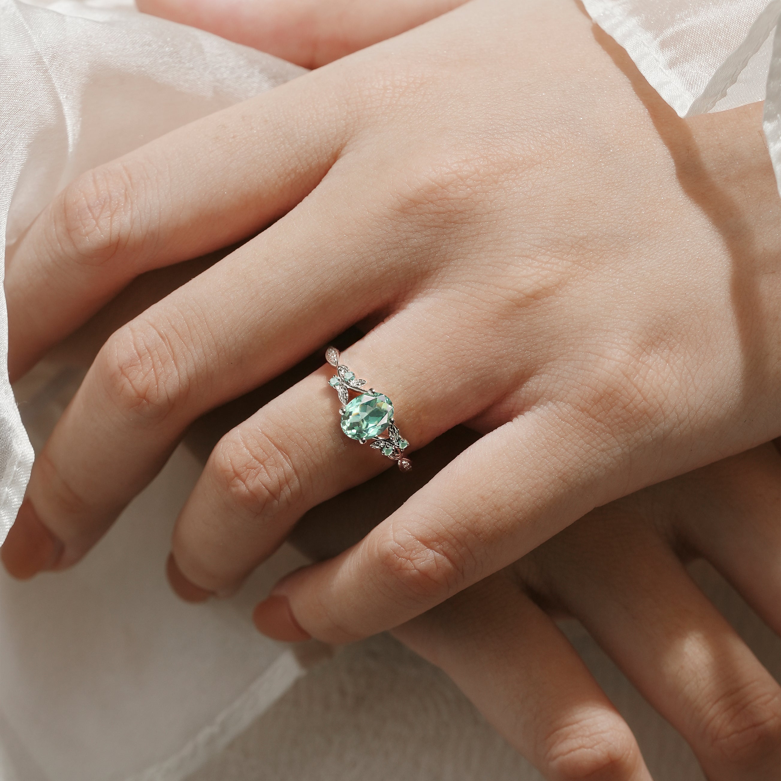 Green sapphire engagement ring on hand with leaf design