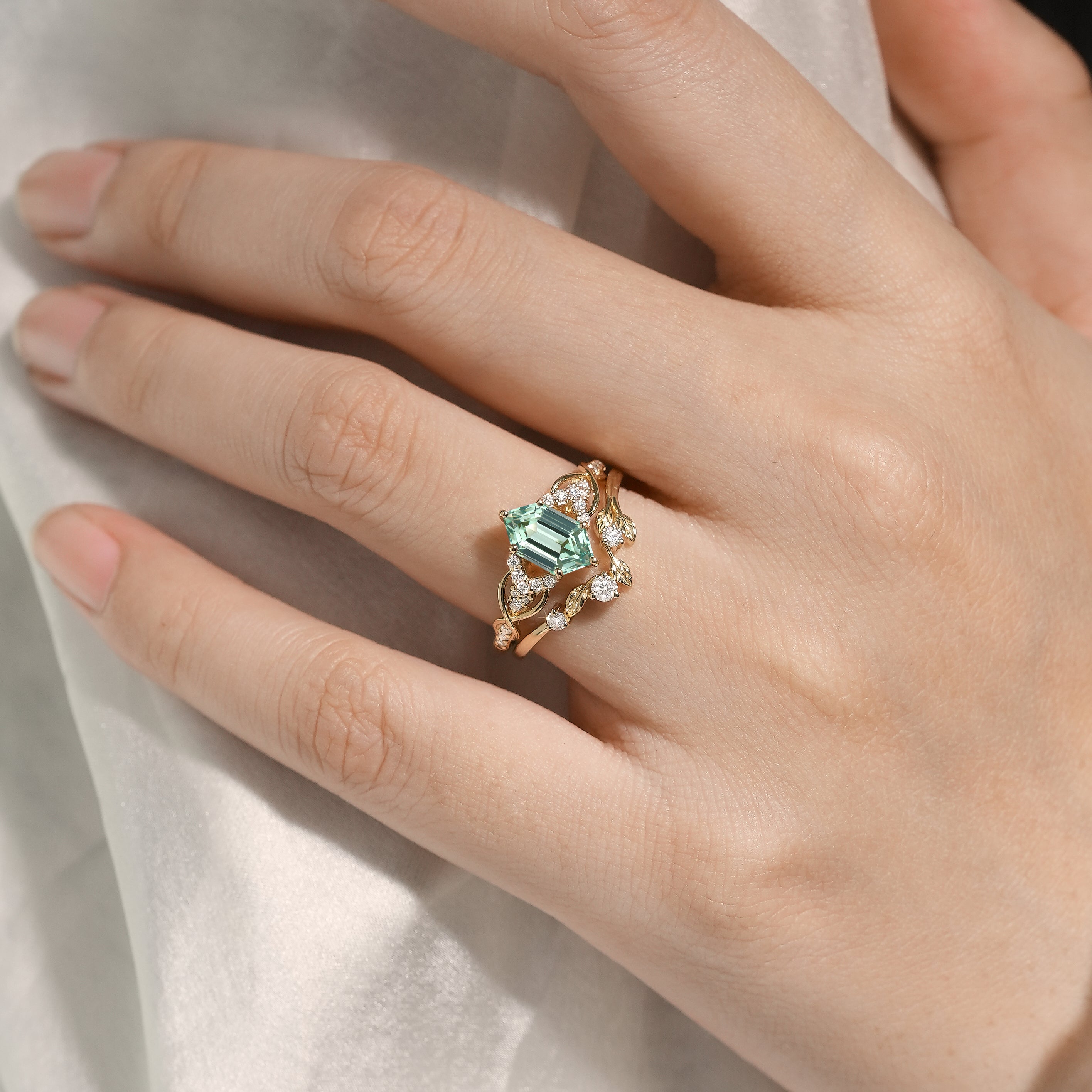Woman's hand wearing green sapphire engagement ring and leaf wedding band