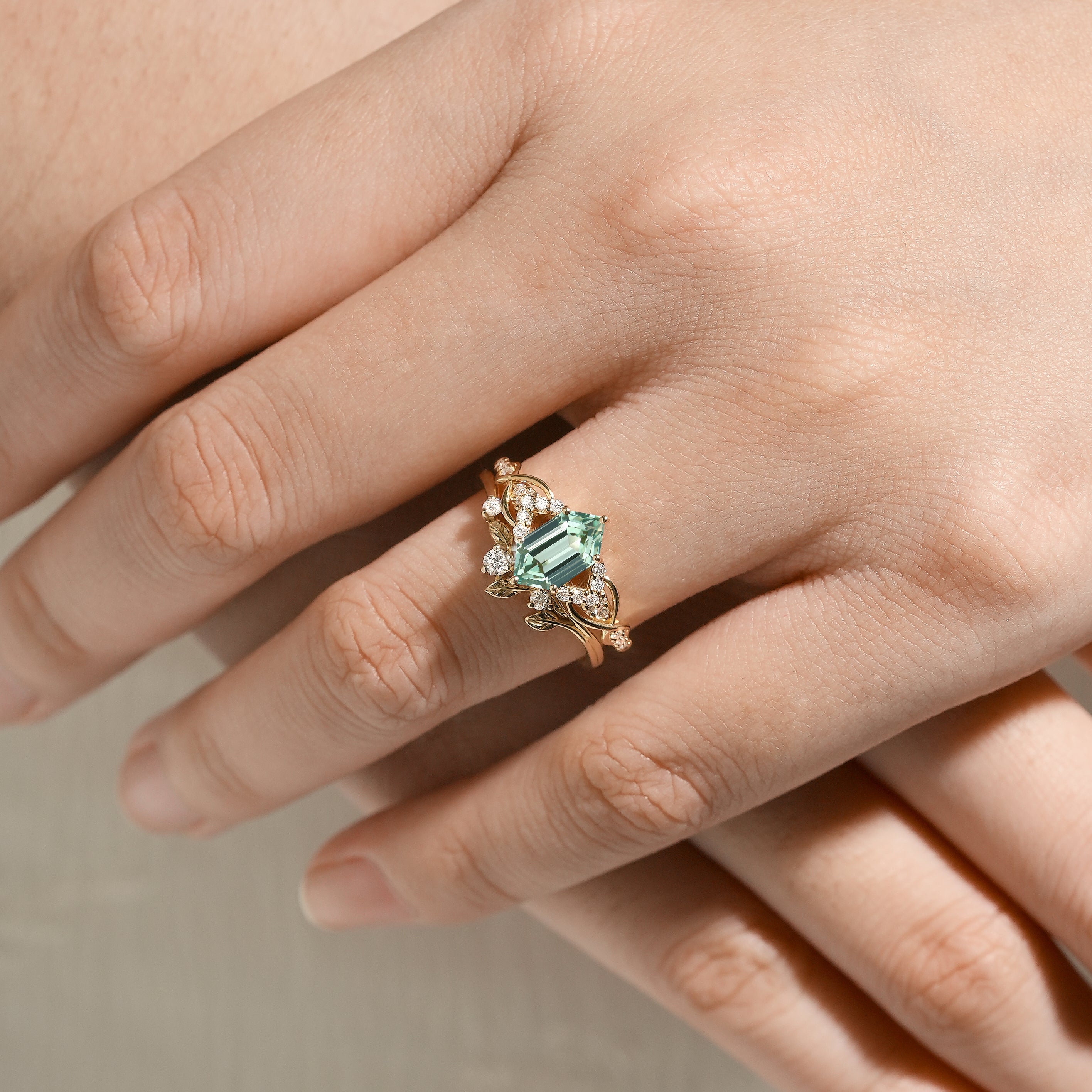 Close-up of a hand wearing nature-inspired green sapphire engagement ring and leaf wedding band