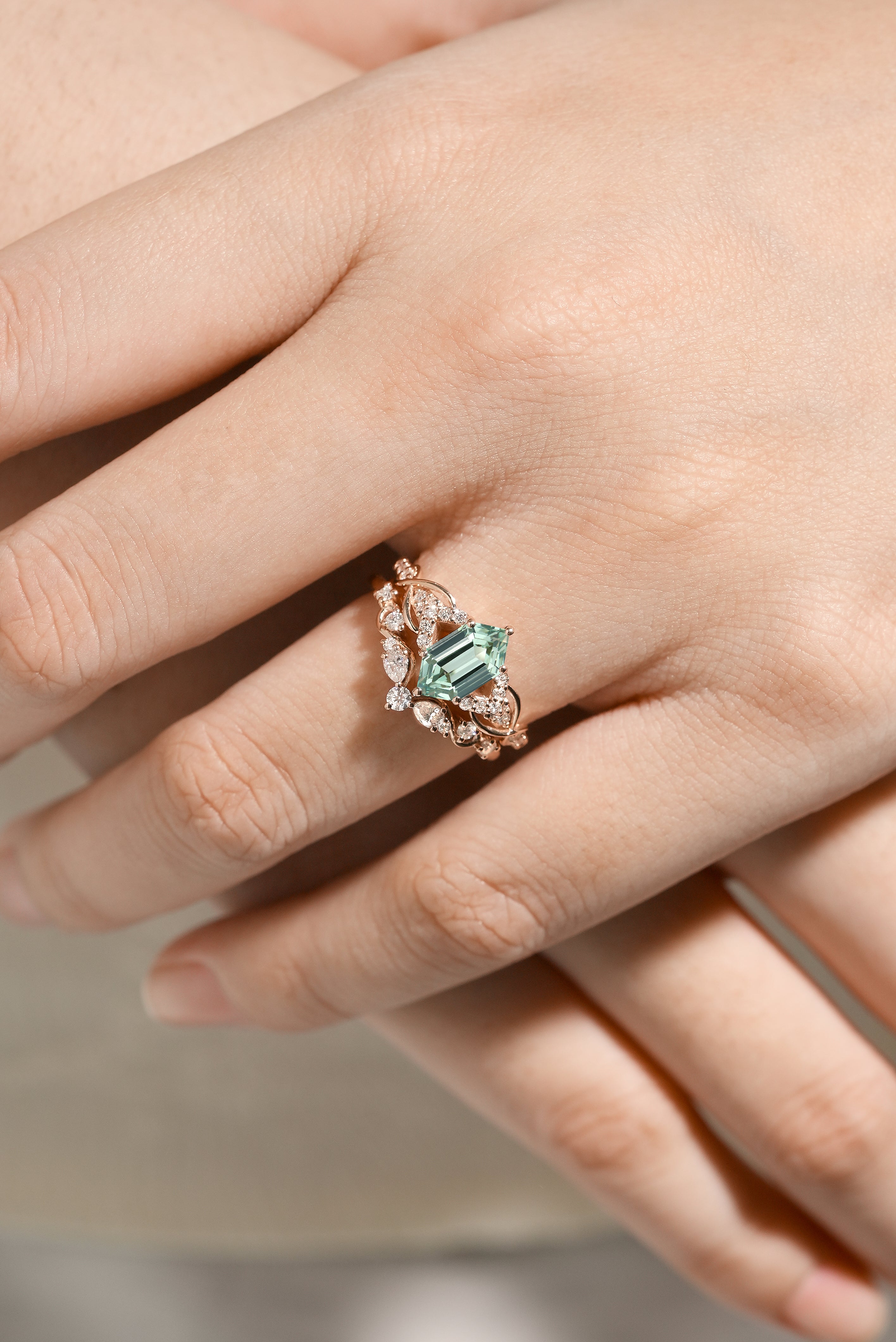 Close-up of a hand wearing a green sapphire and moissanite bridal set ring, nature-inspired