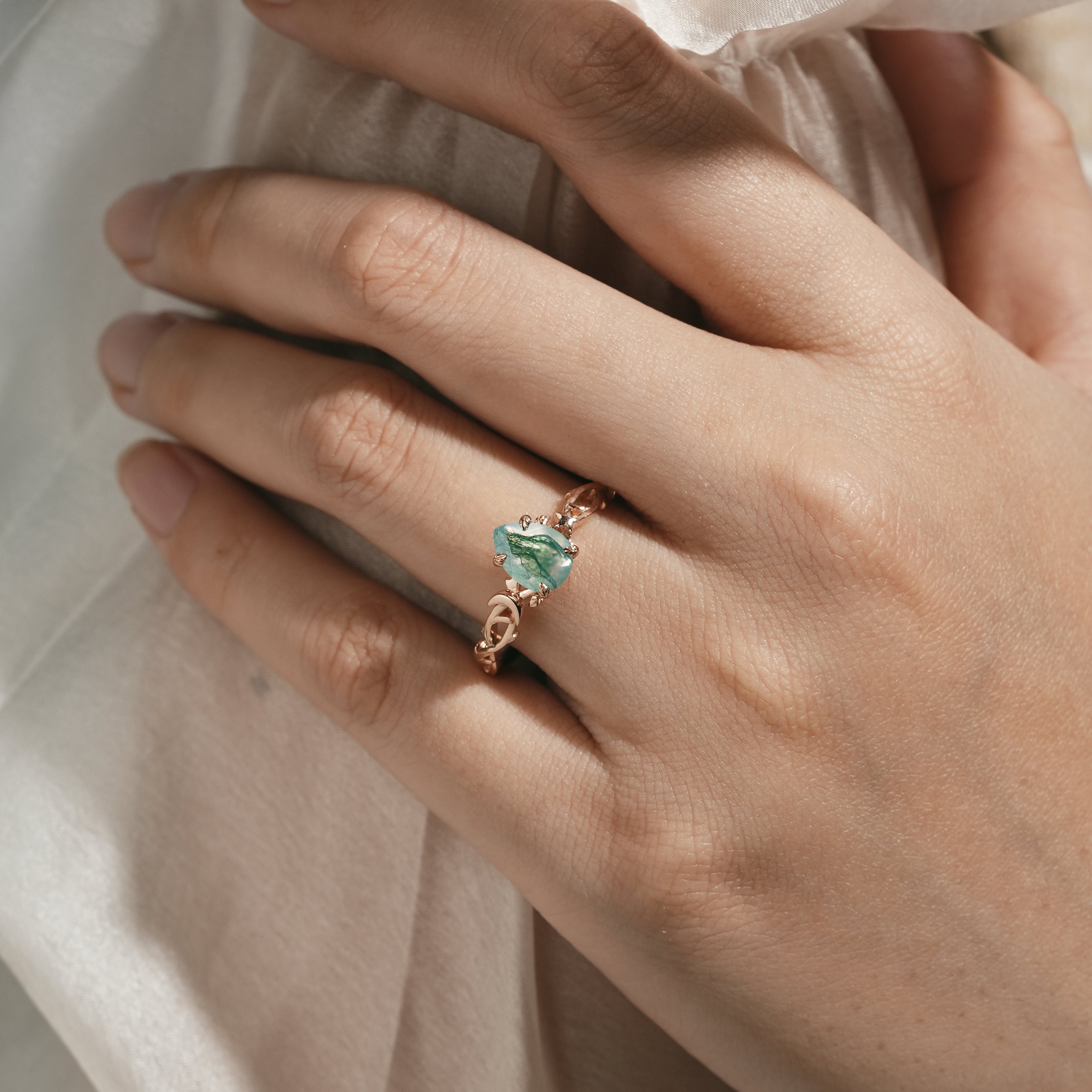 Woman's hand wearing pear cut moss agate engagement ring