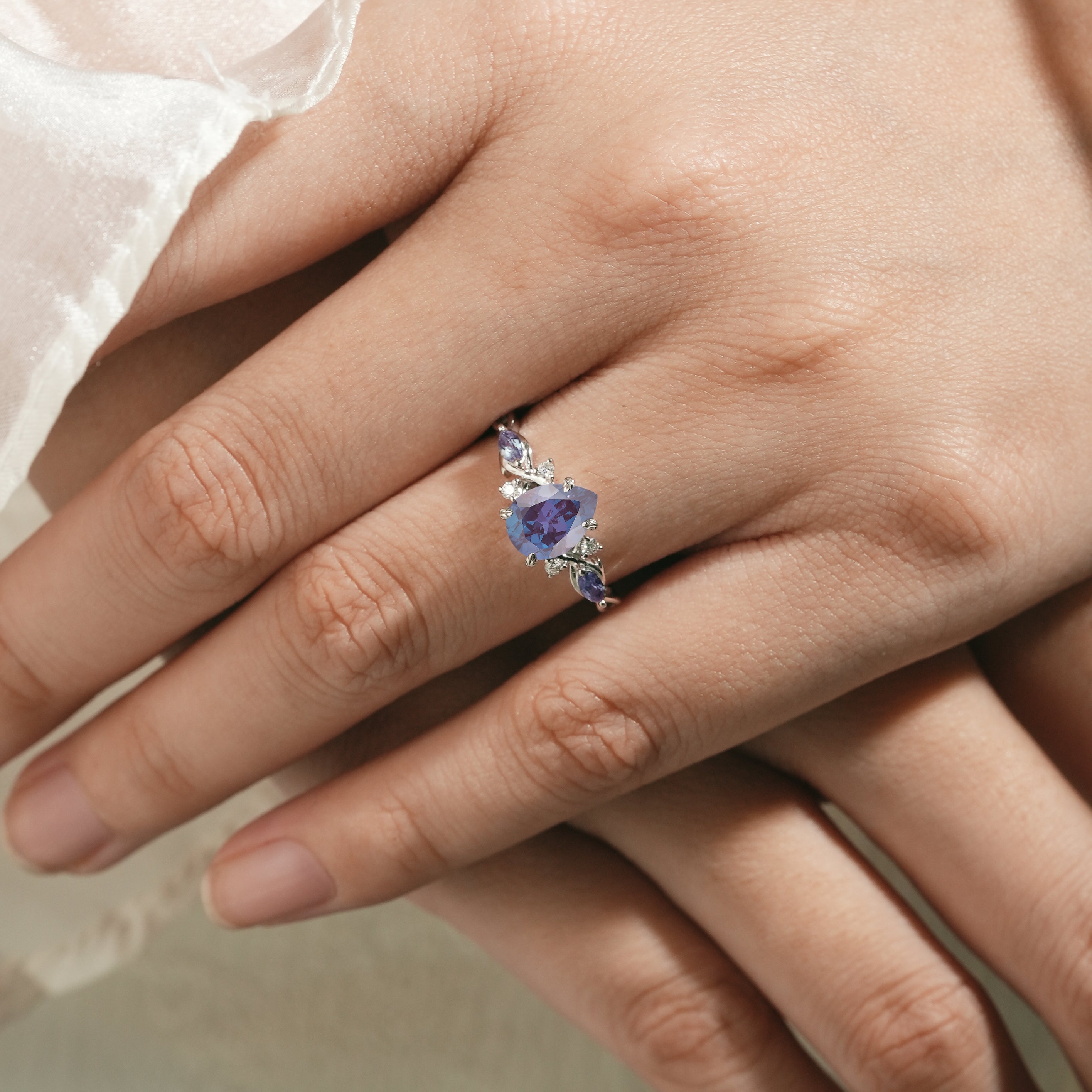 Elegant alexandrite engagement ring with pear-cut center stone on a hand, featuring moissanite accents. Lahela Jewelry.
