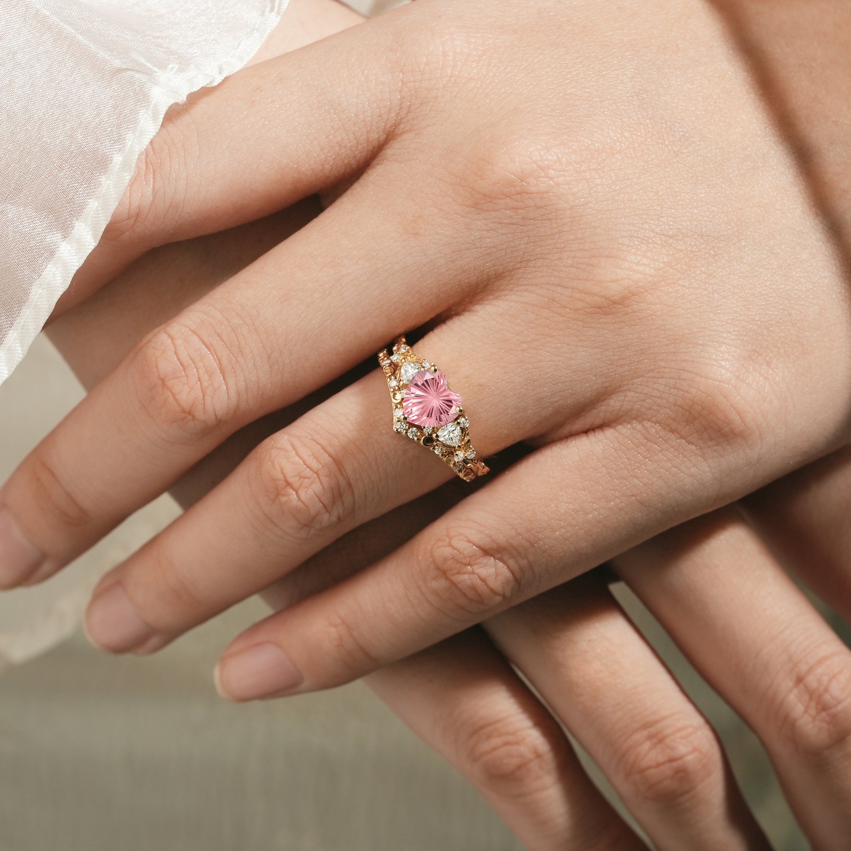 Heart-cut Padparadscha engagement ring on a hand, gold band.