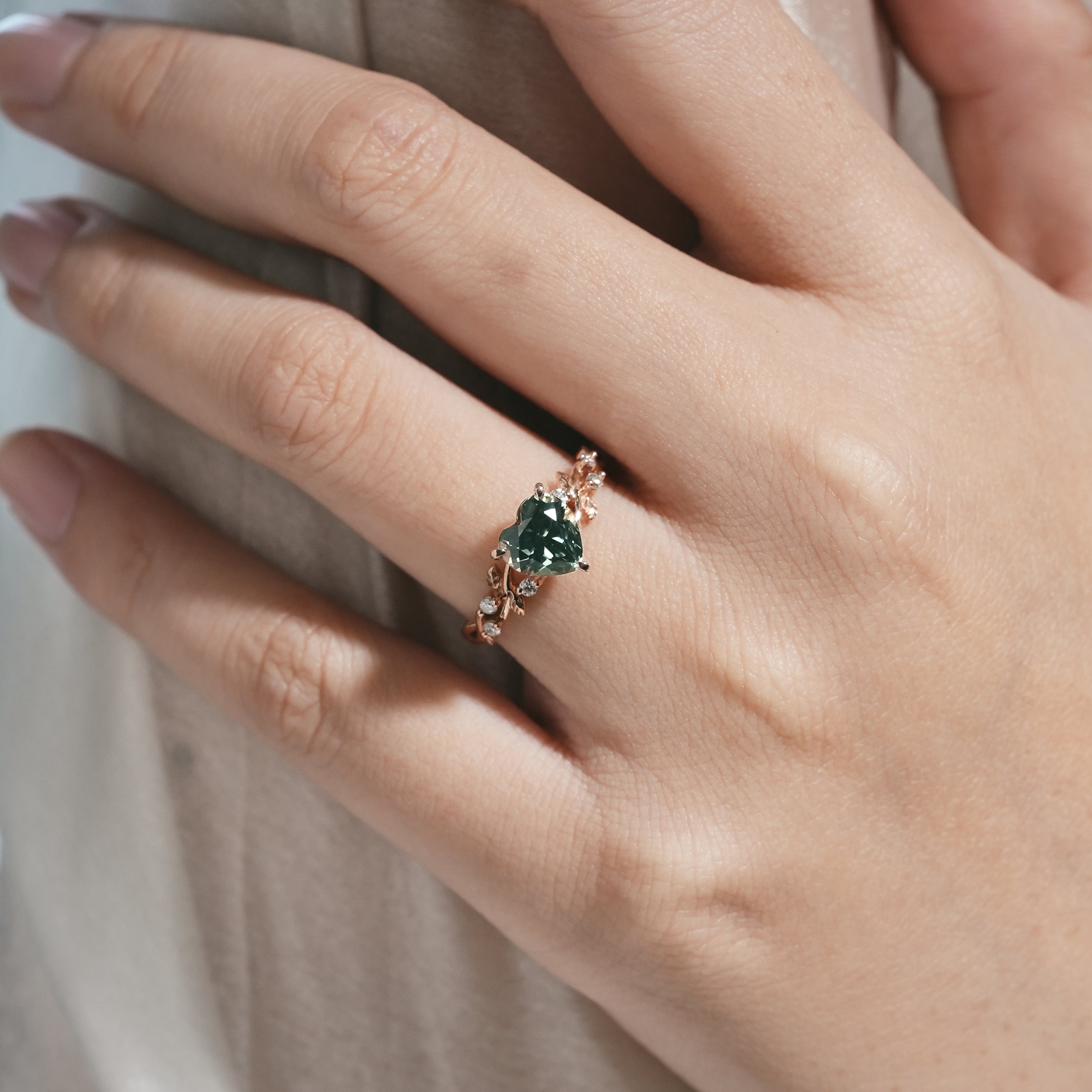 Woman's hand wearing green sapphire leaf engagement ring