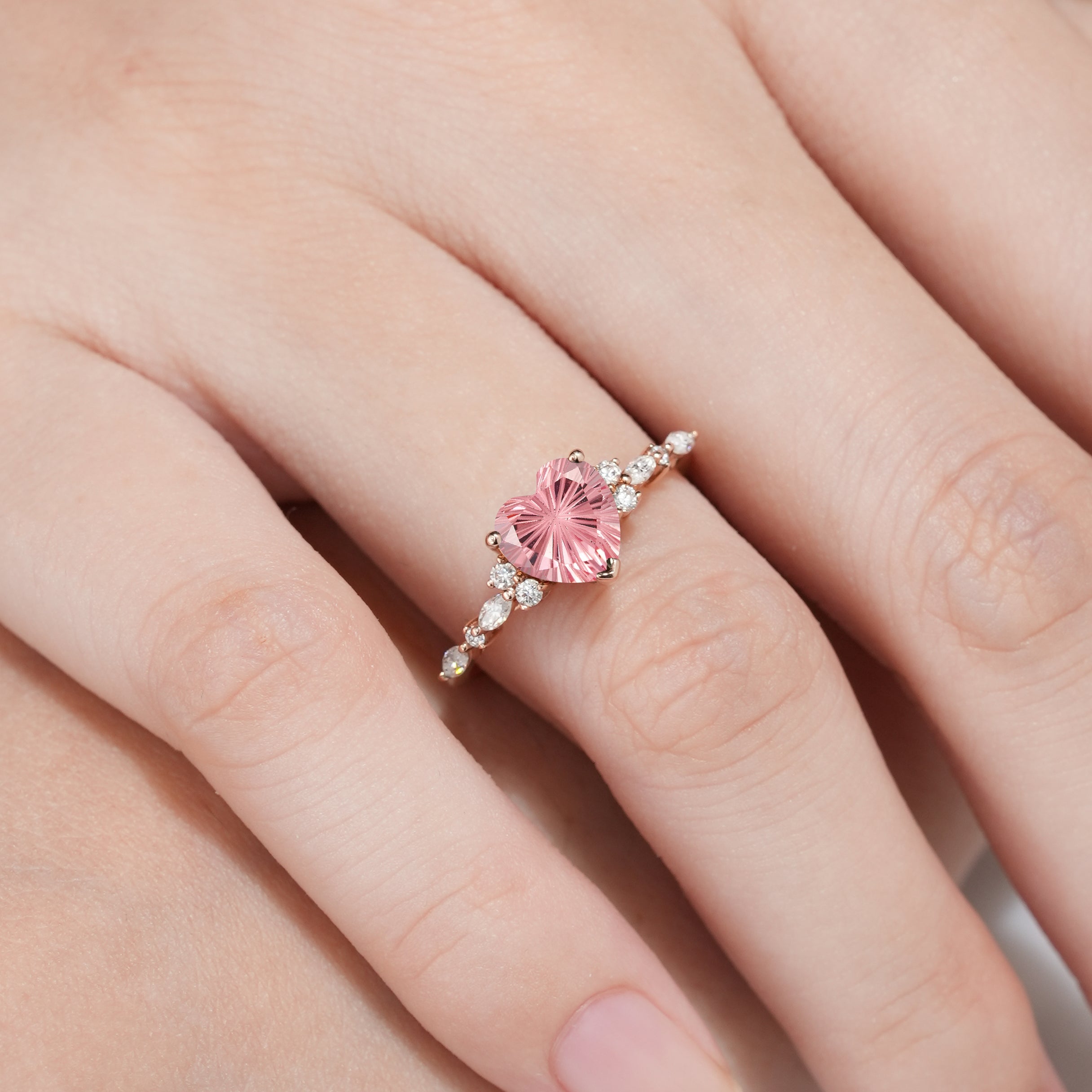 Heart-cut Padparadscha engagement ring on a hand