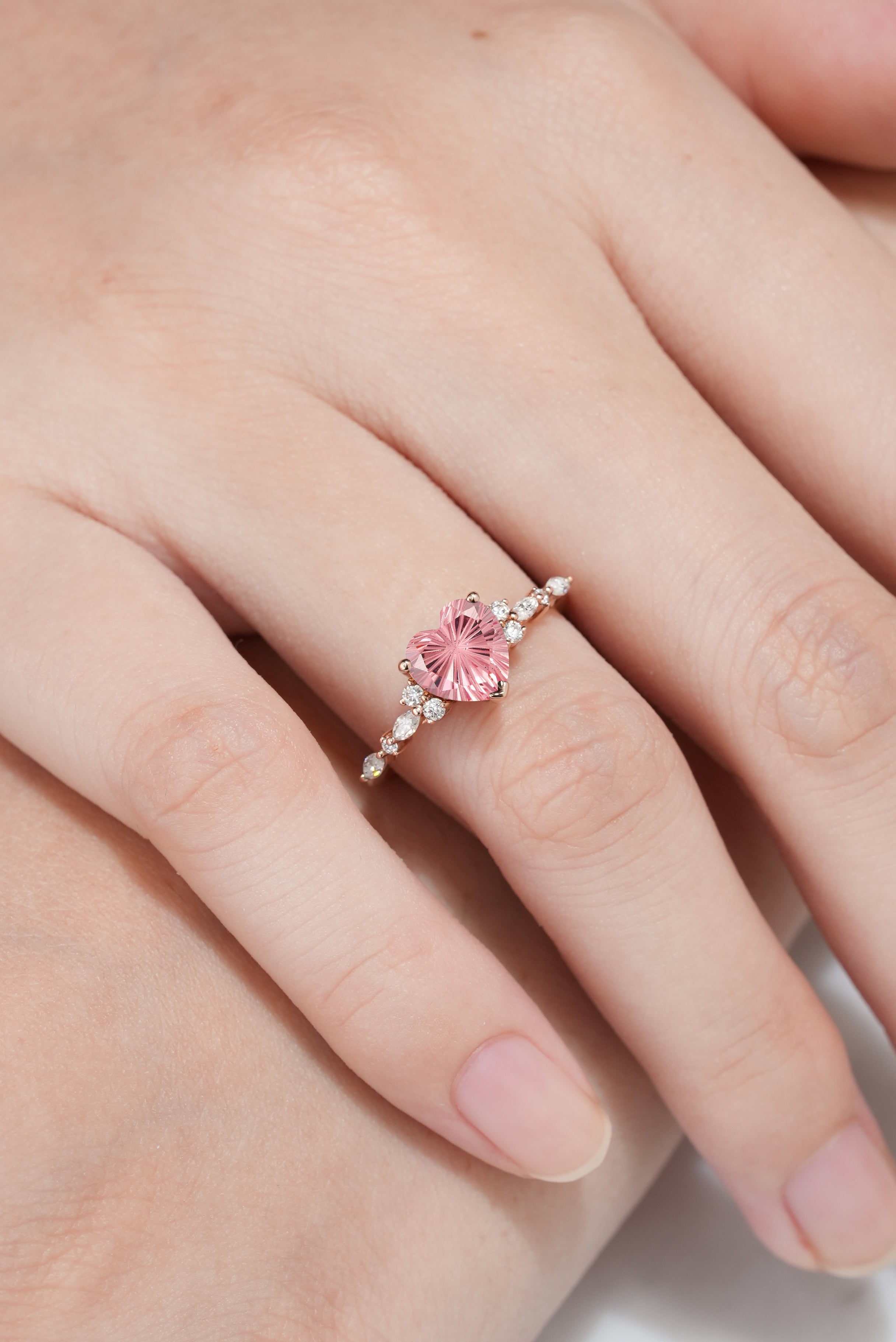 Heart-cut Padparadscha engagement ring on a hand