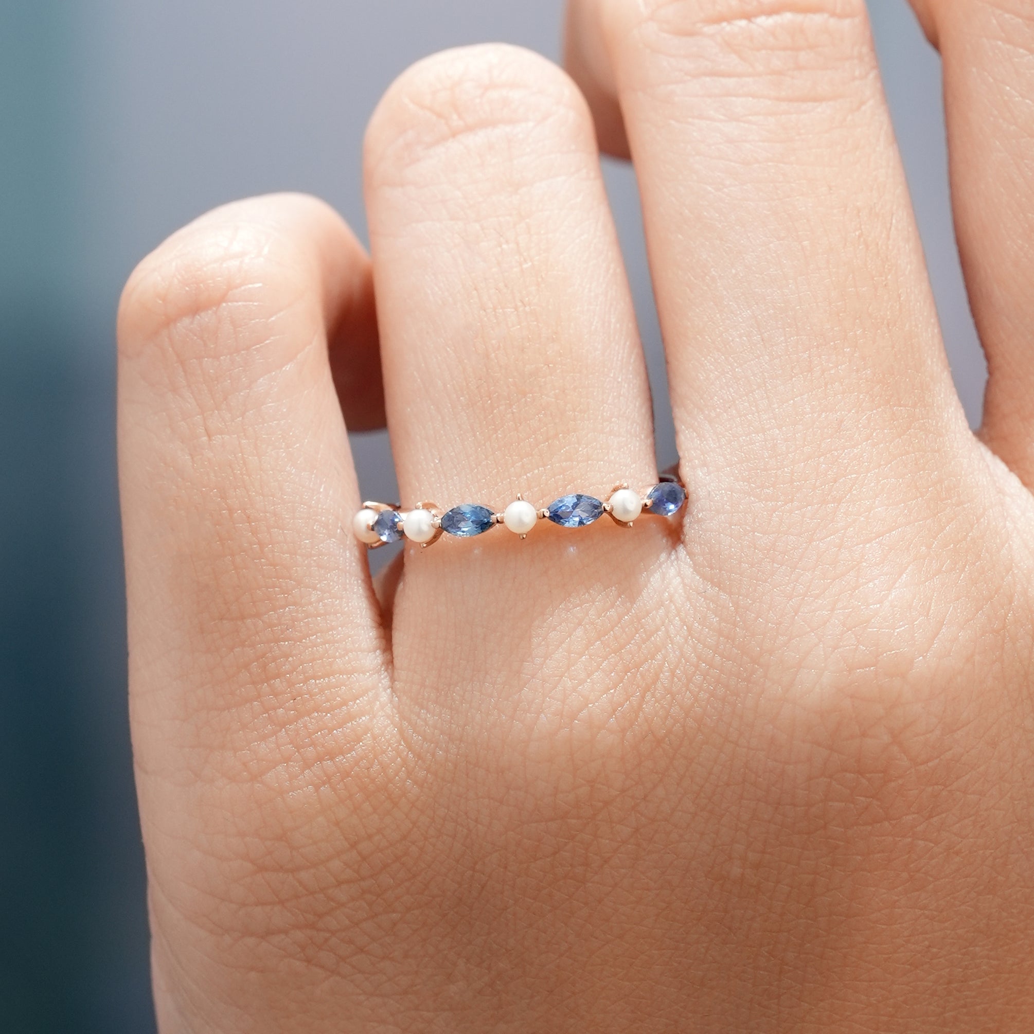 Marquise cut sapphire and pearl wedding band on a finger