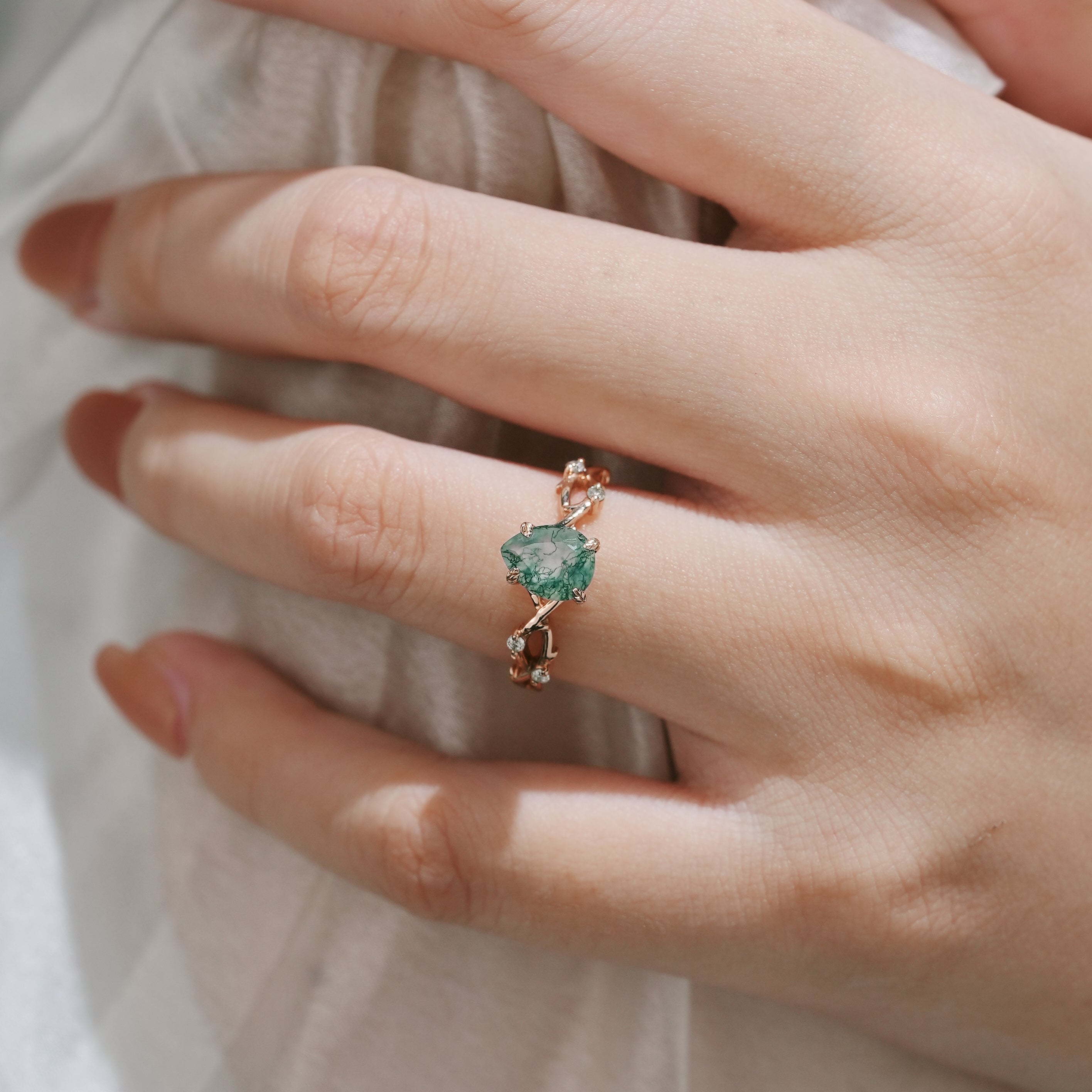 Hand holding a pear cut moss agate ring with vine leaf design