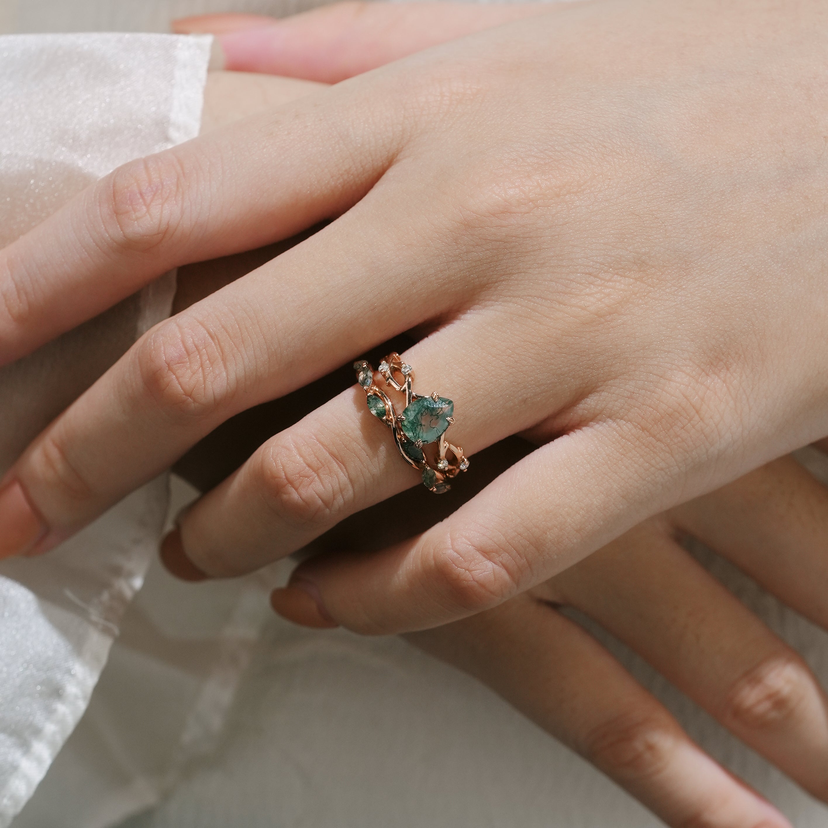 Hand wearing a rose gold moss agate engagement ring with leaf design, accented with moissanite.