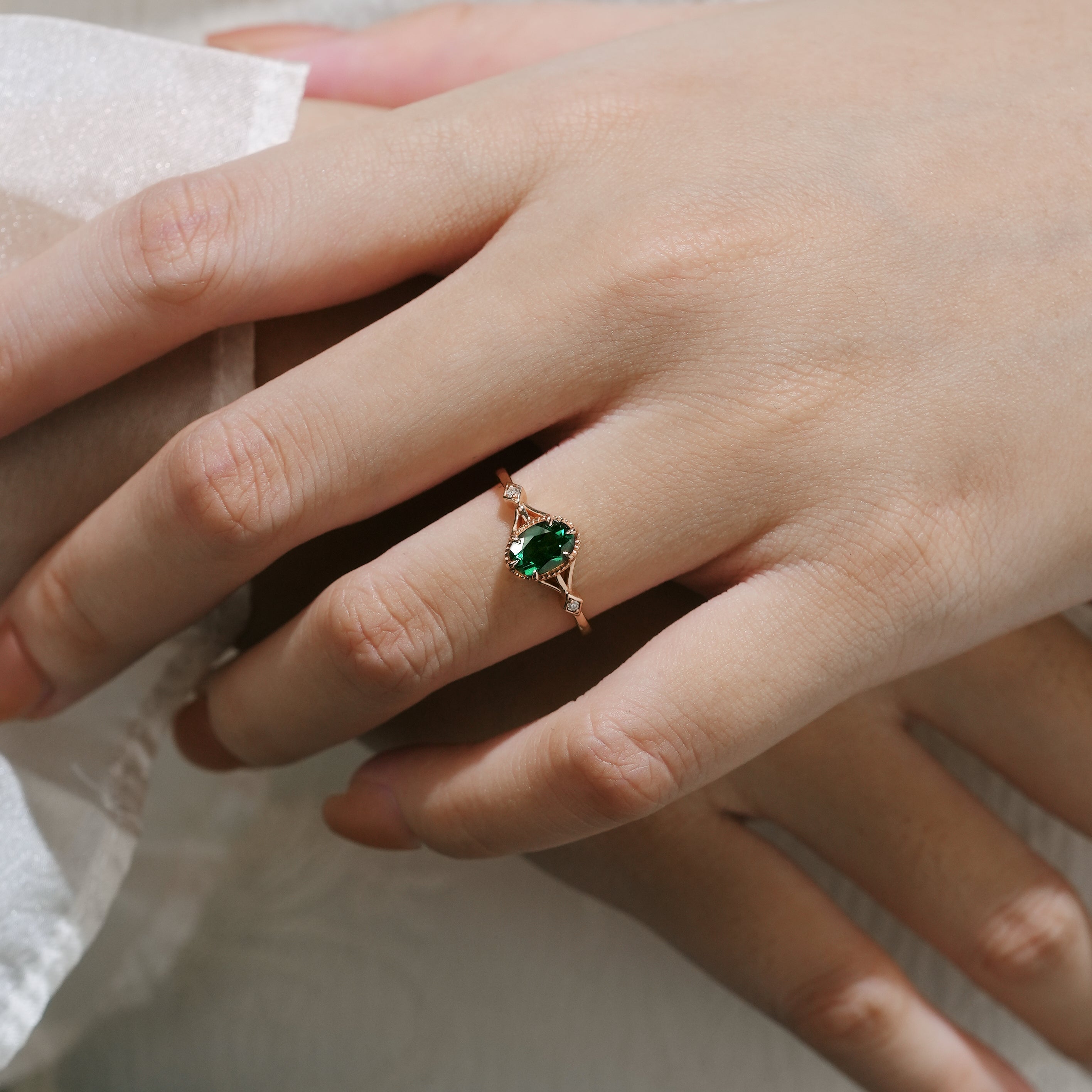 Oval emerald engagement ring on finger, nature-inspired rose gold design
