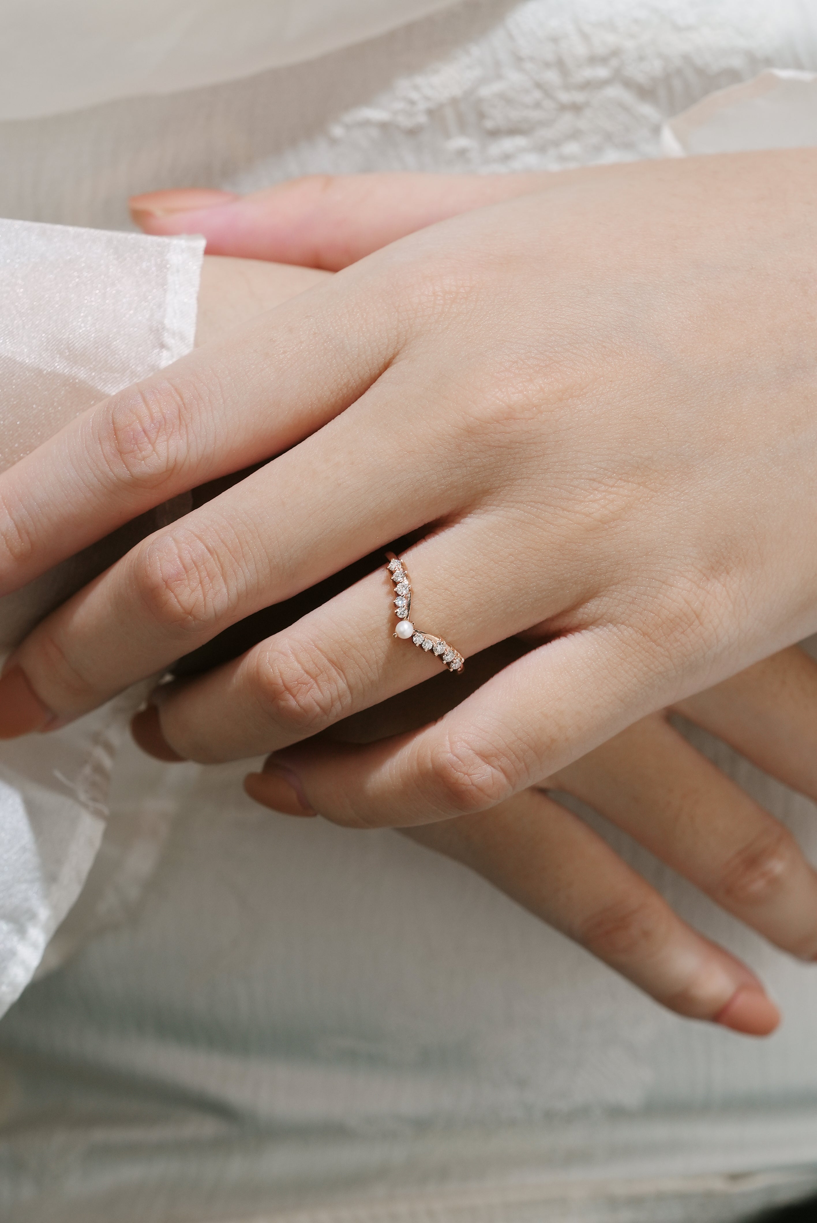 Woman's hand wearing rose gold curved wedding band with moissanite and pearl accents, bridal ring set.