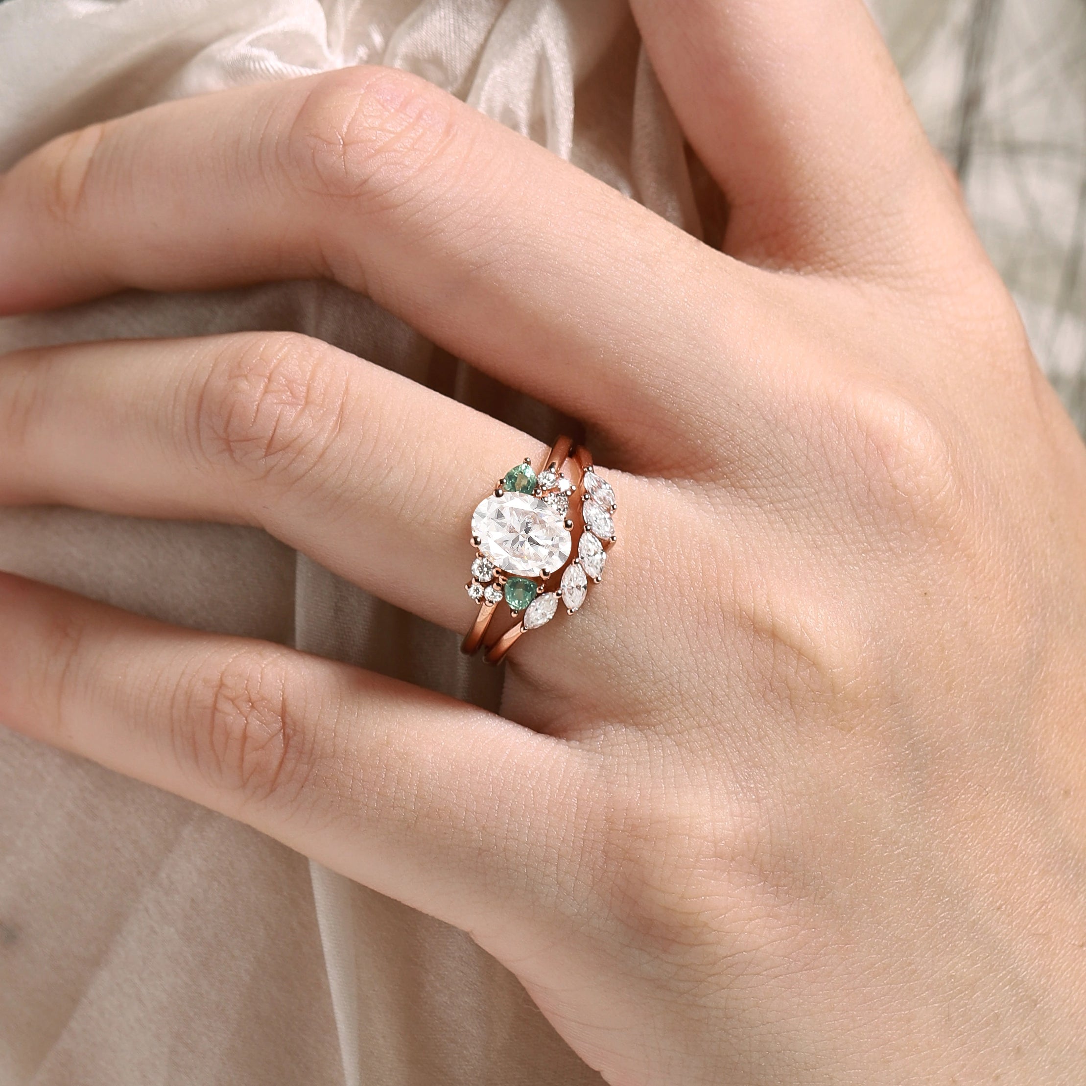 Rose gold oval moissanite bridal set with spinel accents. Vintage-style engagement ring and wedding band on hand.