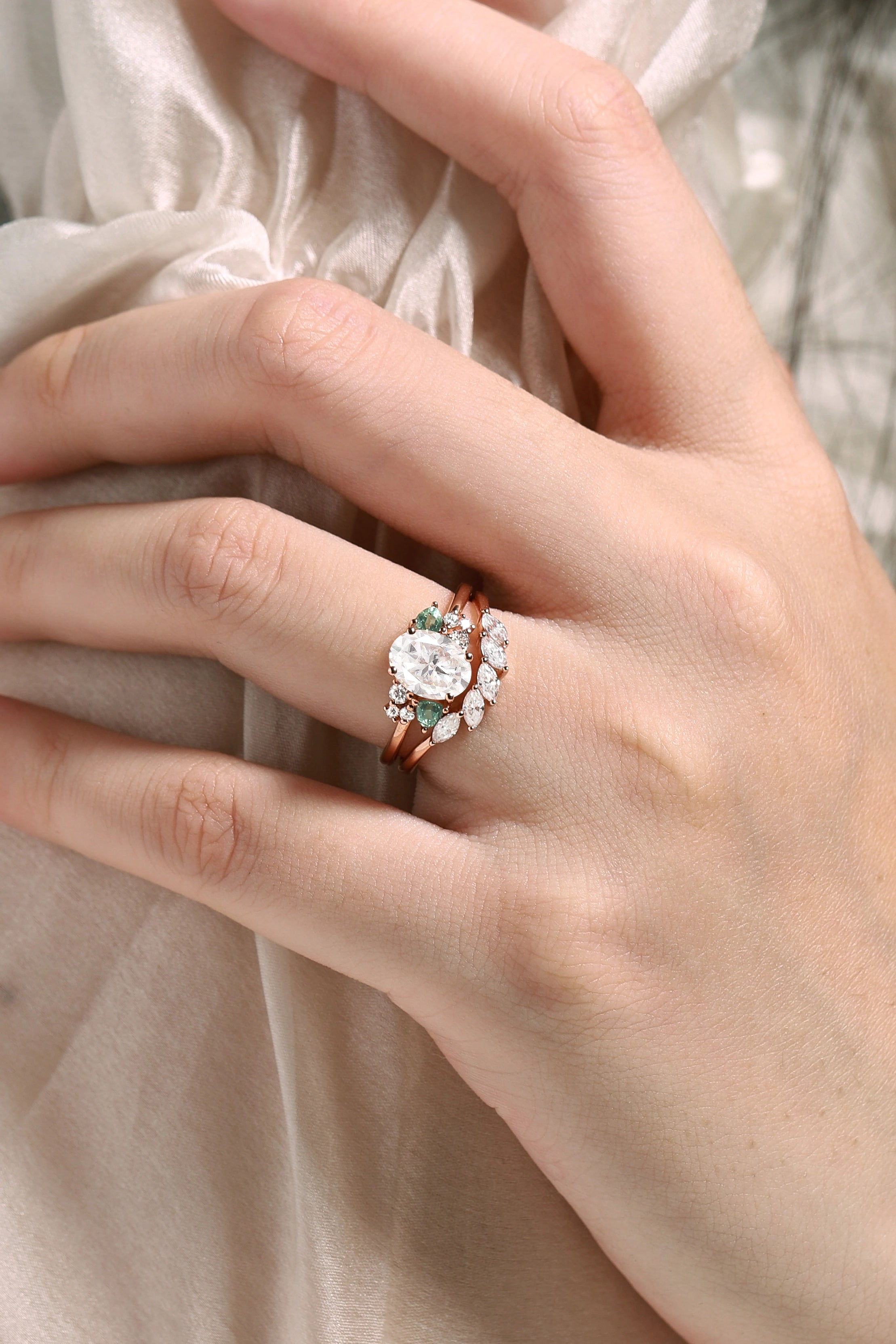 Rose gold oval moissanite bridal set with spinel accents. Vintage-style engagement ring and wedding band on hand.