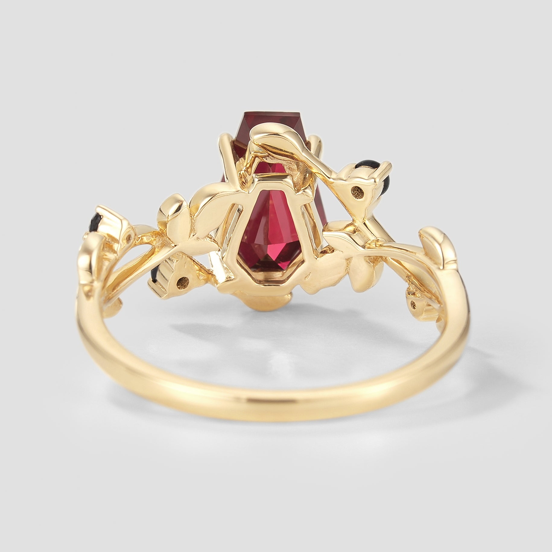 Nature-inspired gold ring with coffin-cut ruby and leaf accents.