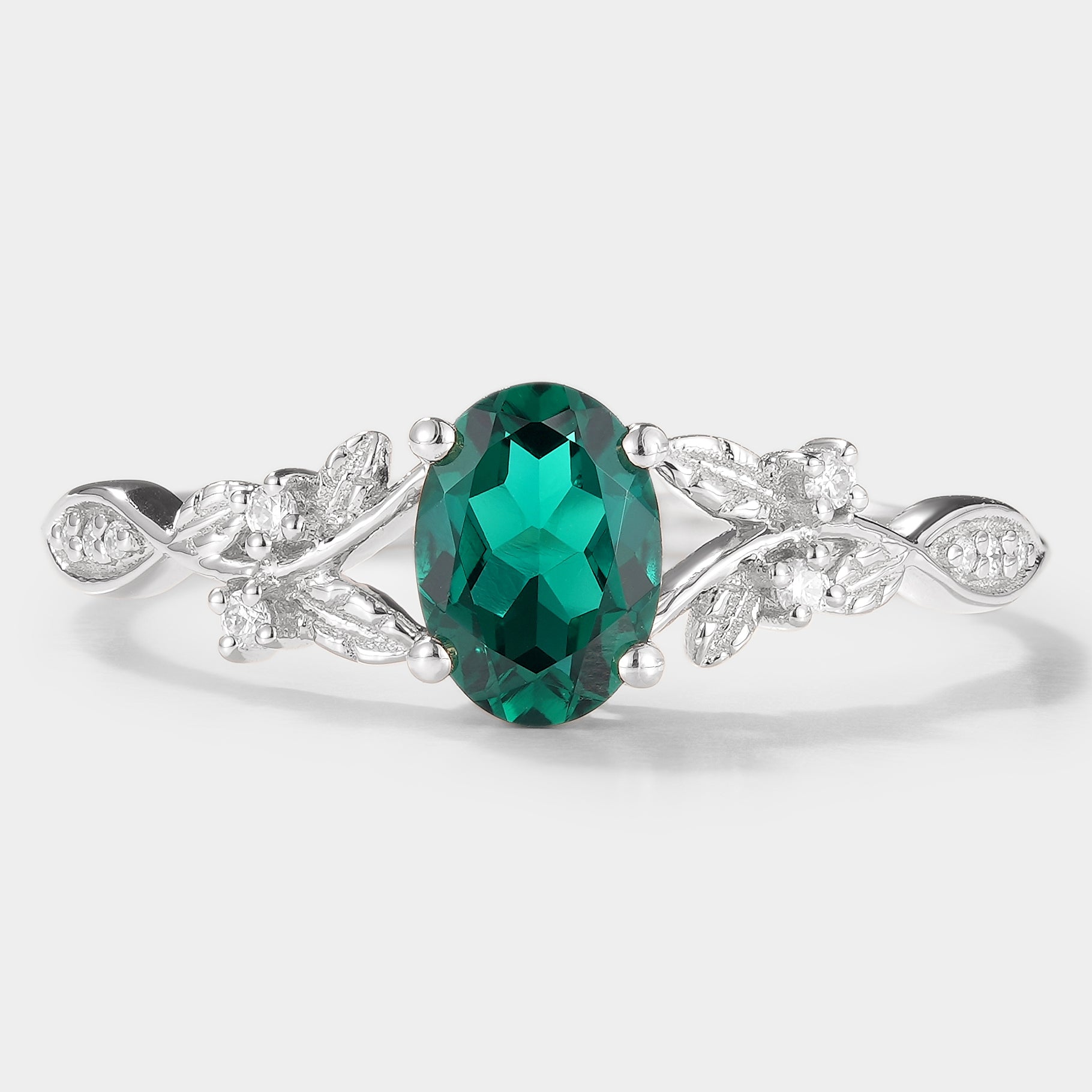 Oval lab grown emerald engagement ring with leaf design and moissanite accents. Vintage-style ring.