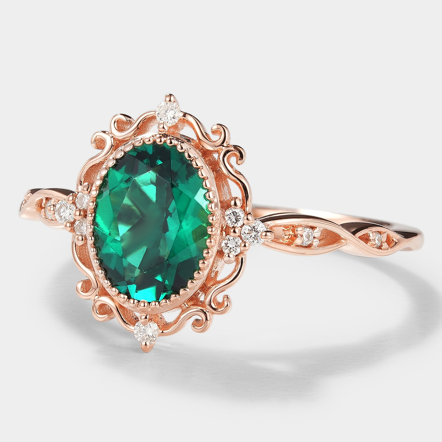 Vintage rose gold emerald engagement ring with moissanite accents. Lab-grown emerald ring with intricate filigree detailing.