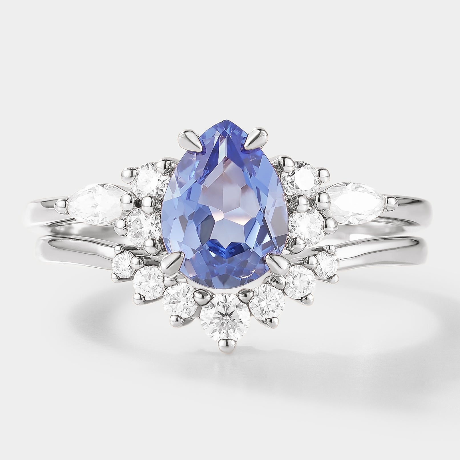 Pear cut cornflower sapphire engagement ring with a curved moissanite wedding band. Bridal set in white gold
