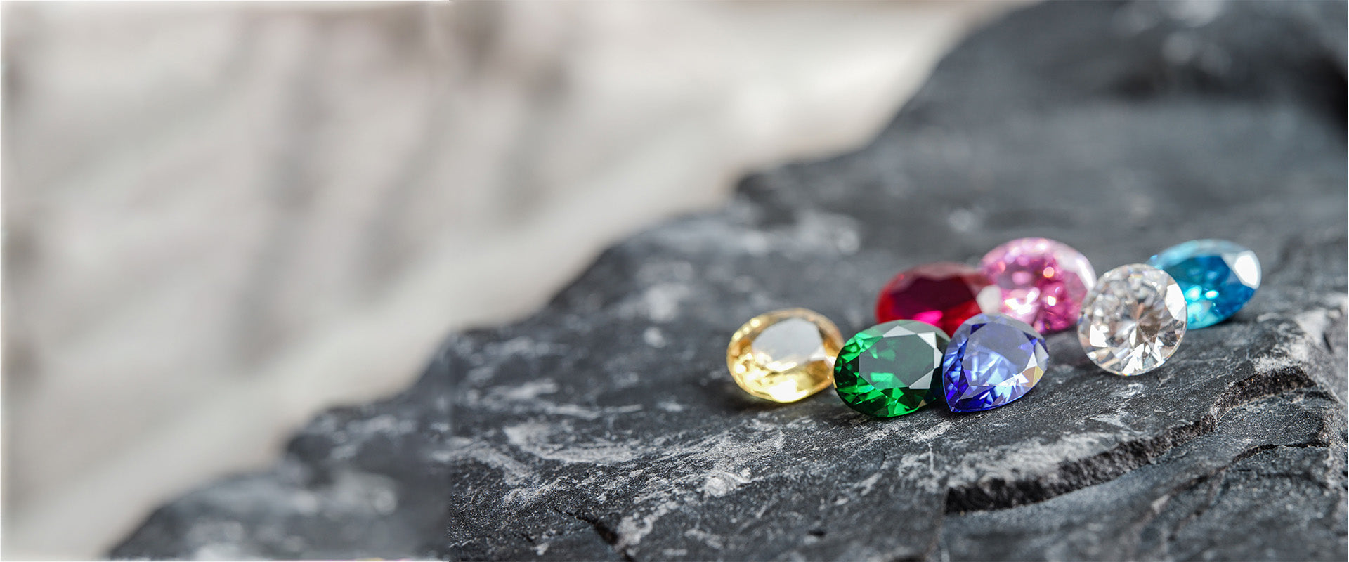 Vibrant gemstones in yellow, green, blue, pink, and red rest on a dark, textured rock surface.