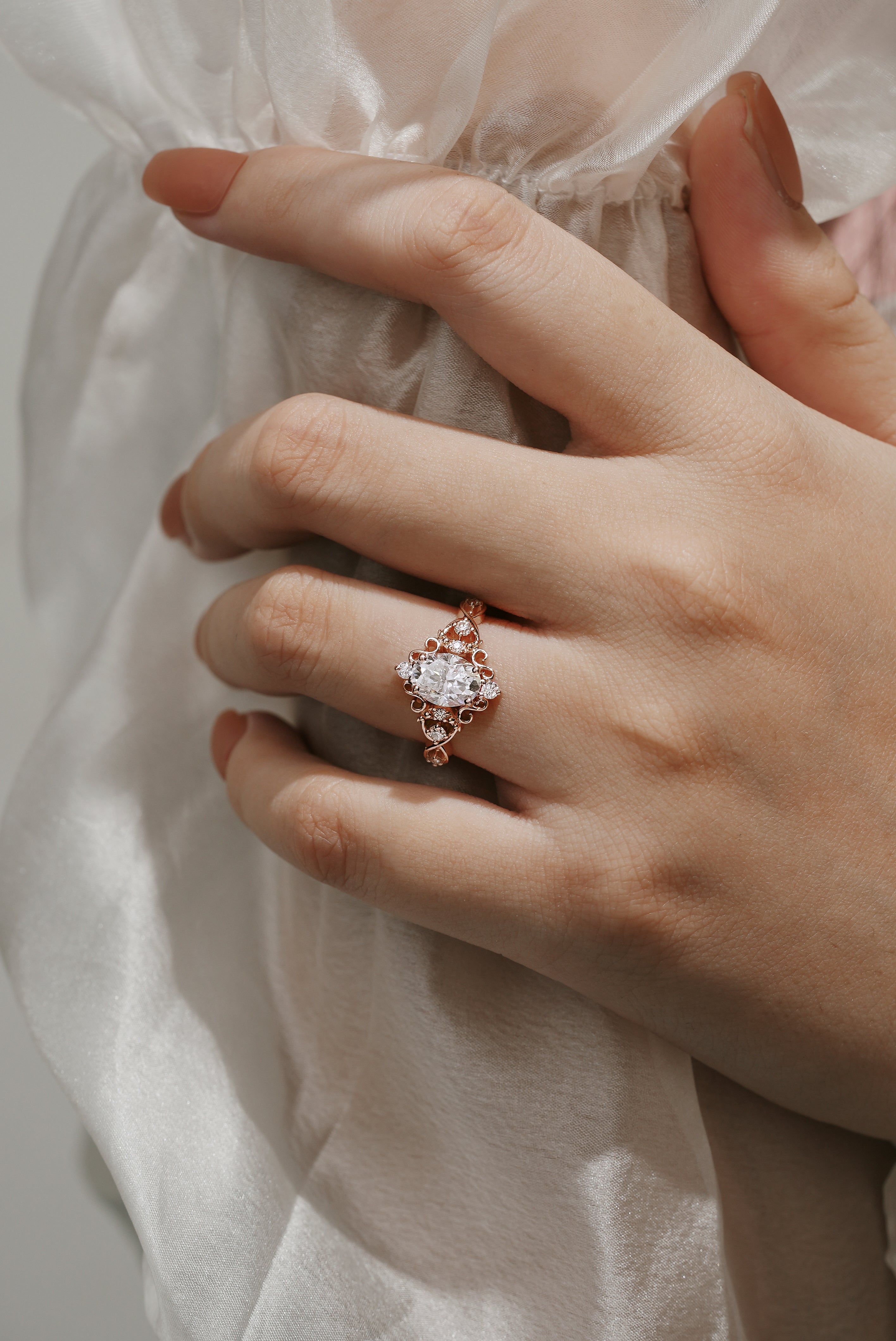 Rose gold vintage engagement ring with oval moissanite center stone and accents on a hand. Bridal jewelry.