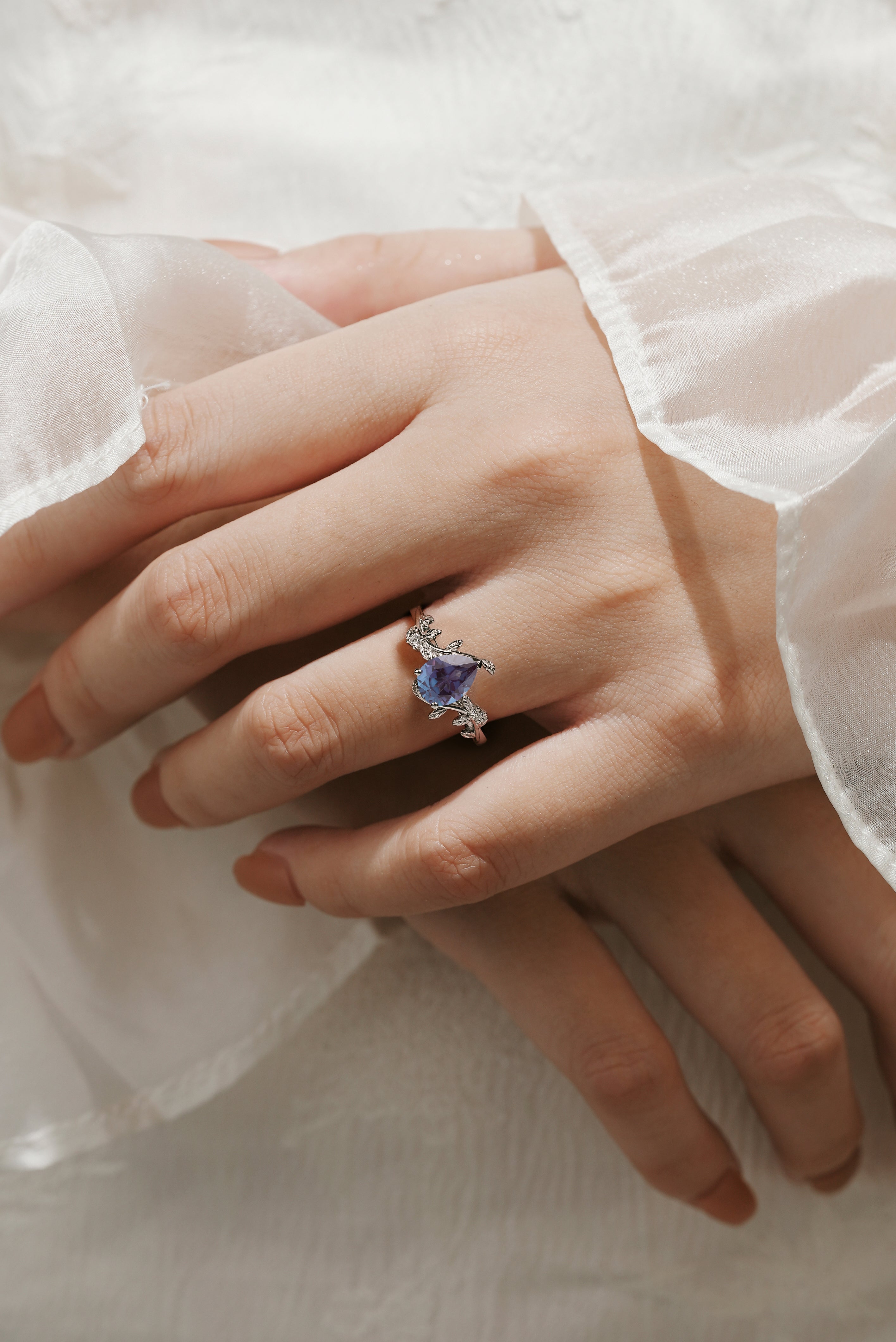 Pear cut alexandrite leaf engagement ring on finger. White gold and moissanite accents, vintage style bridal jewelry