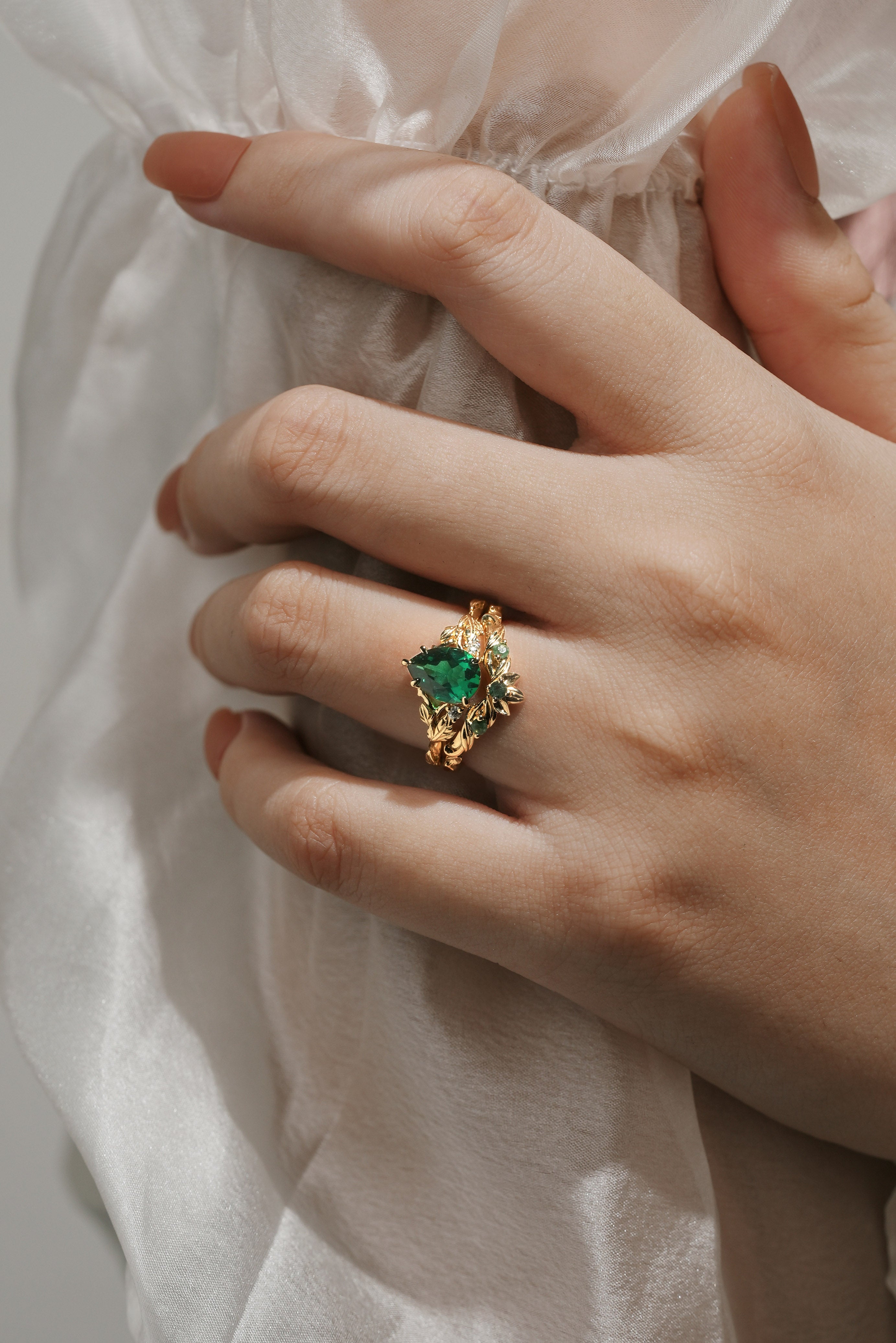 Woman's hand wearing a gold pear-cut emerald leaf bridal set; wedding and engagement ring