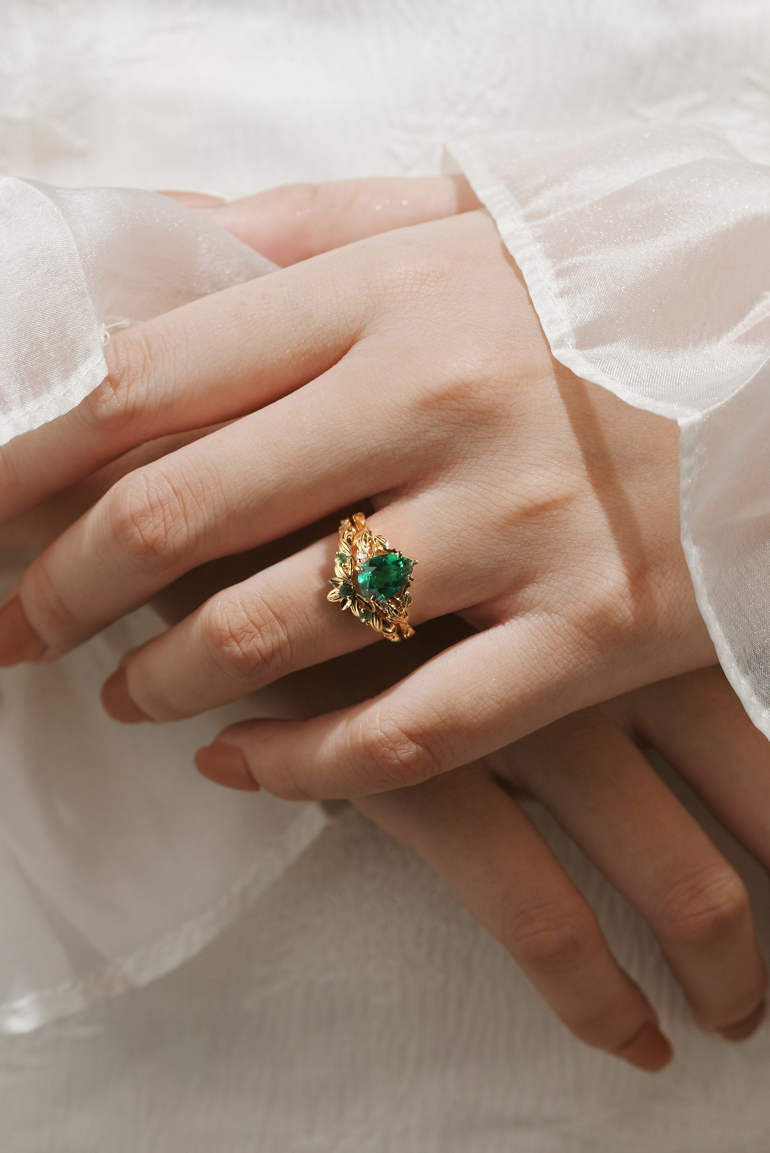Woman's hand wearing a solid gold pear cut emerald leaf engagement ring. Vintage bridal set.