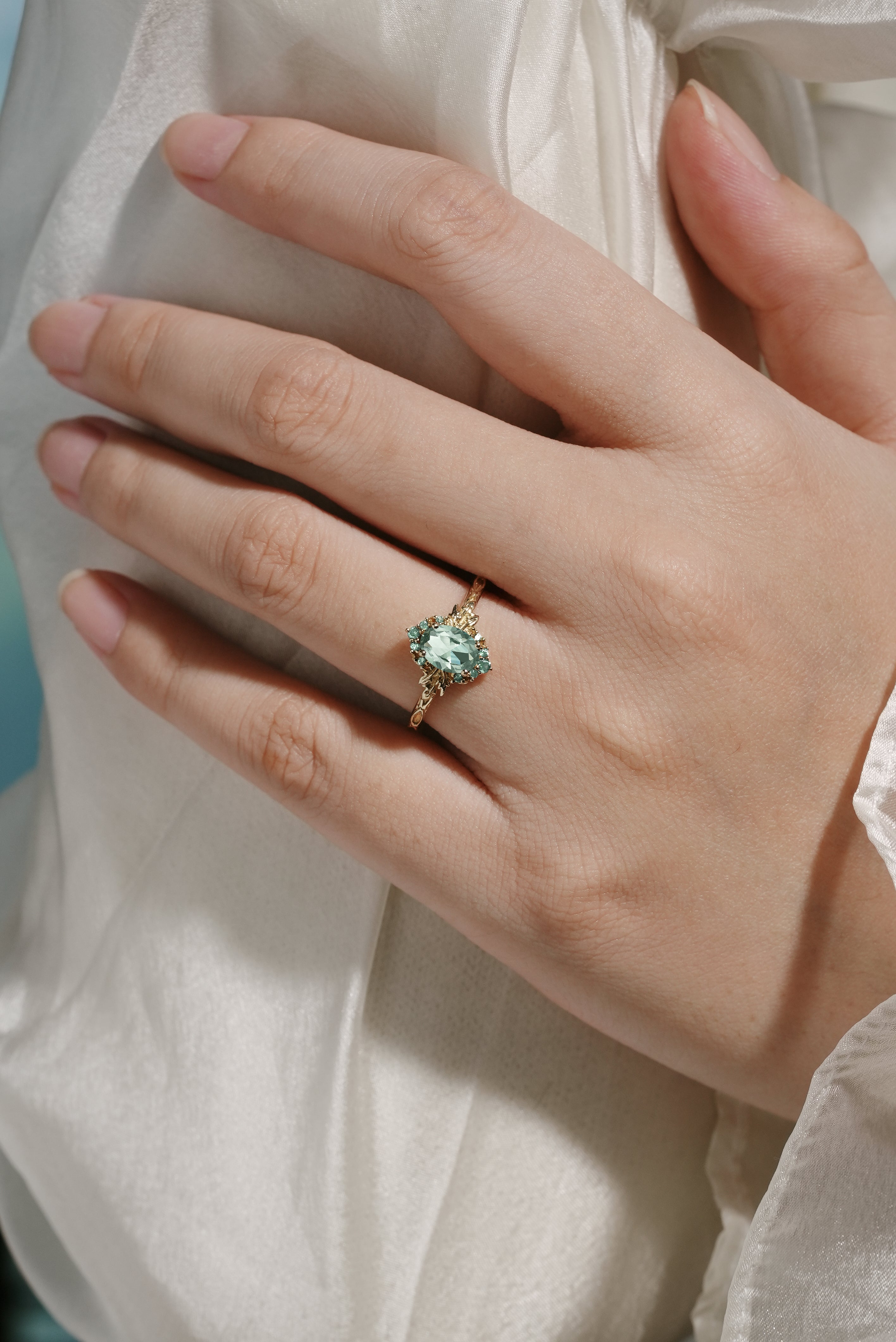 Oval green sapphire engagement ring with leaf design on a hand, gold band, bridal set