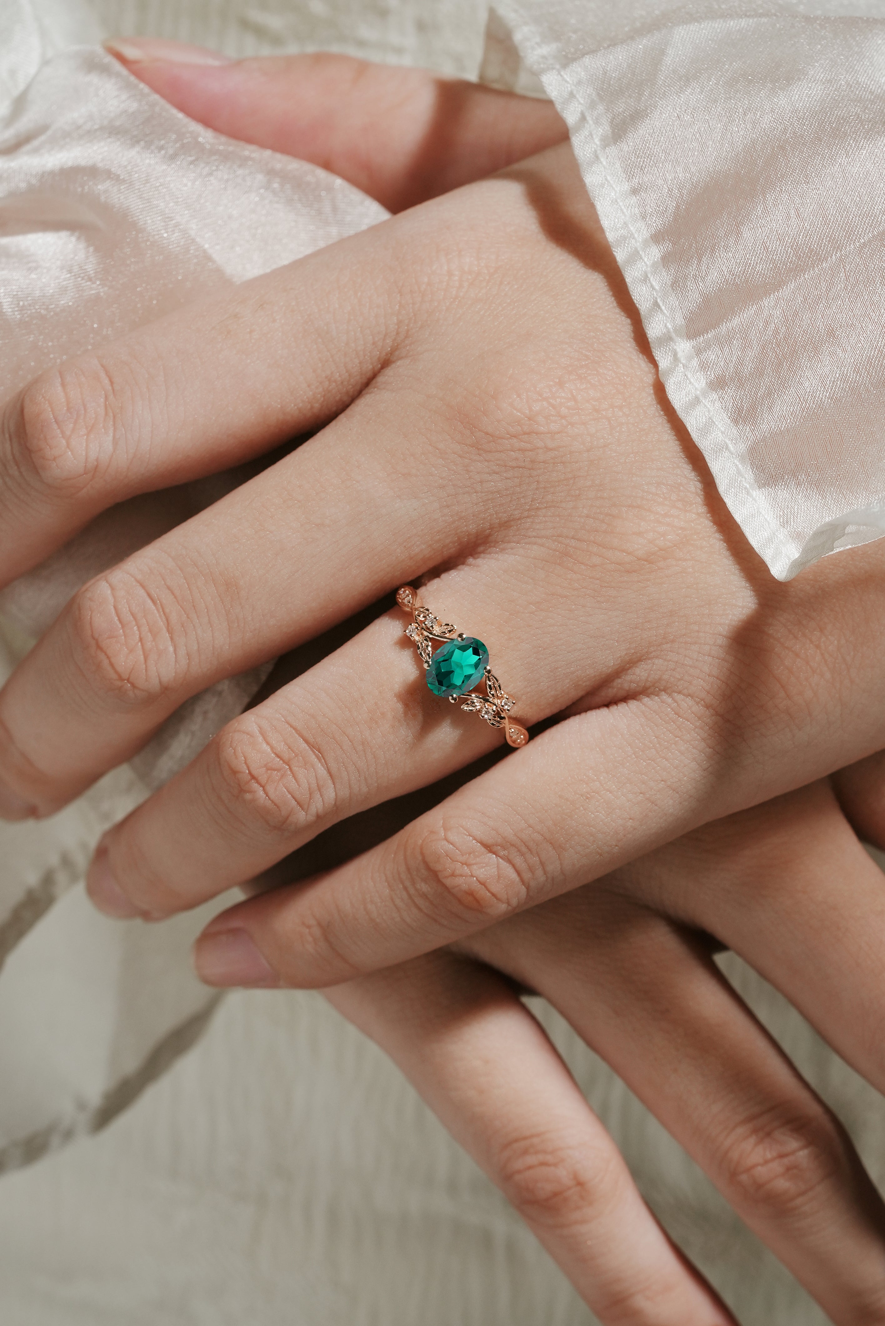 Rose gold oval lab grown emerald engagement ring with leaf design on a hand. Vintage-style wedding ring.