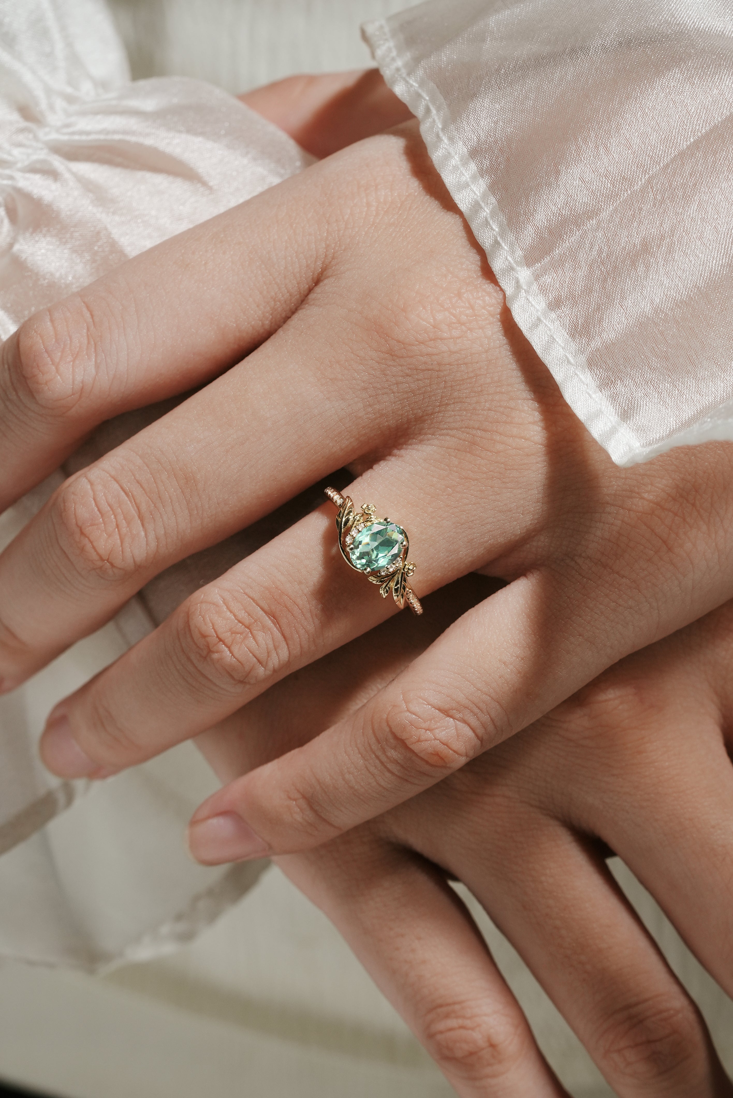 Oval green sapphire engagement ring with leaf and flower accents on a hand, Lahela Jewelry