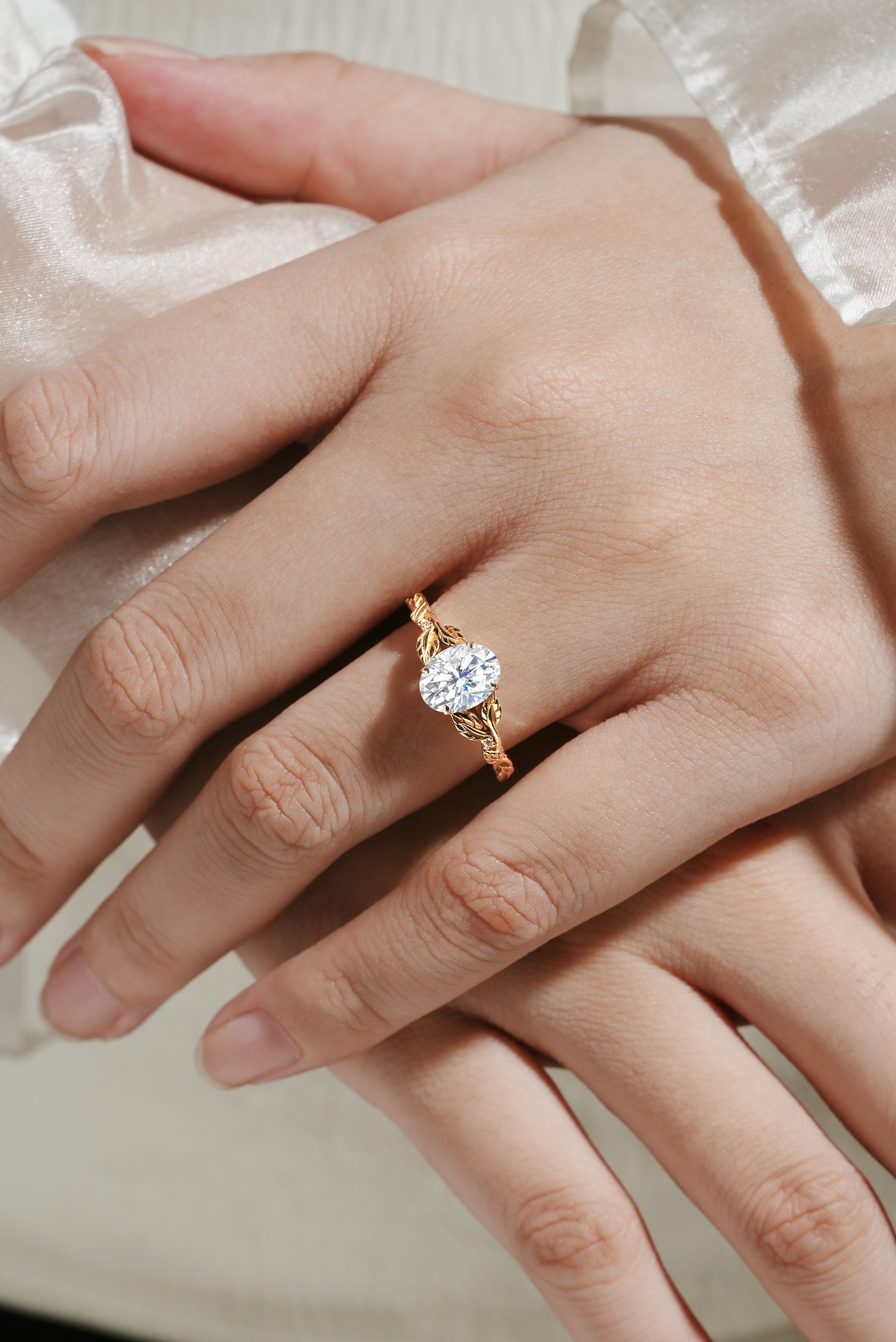Oval moissanite engagement ring with leaf band, gold. Ideal for bridal, wedding. Featuring a beautiful design on a hand.