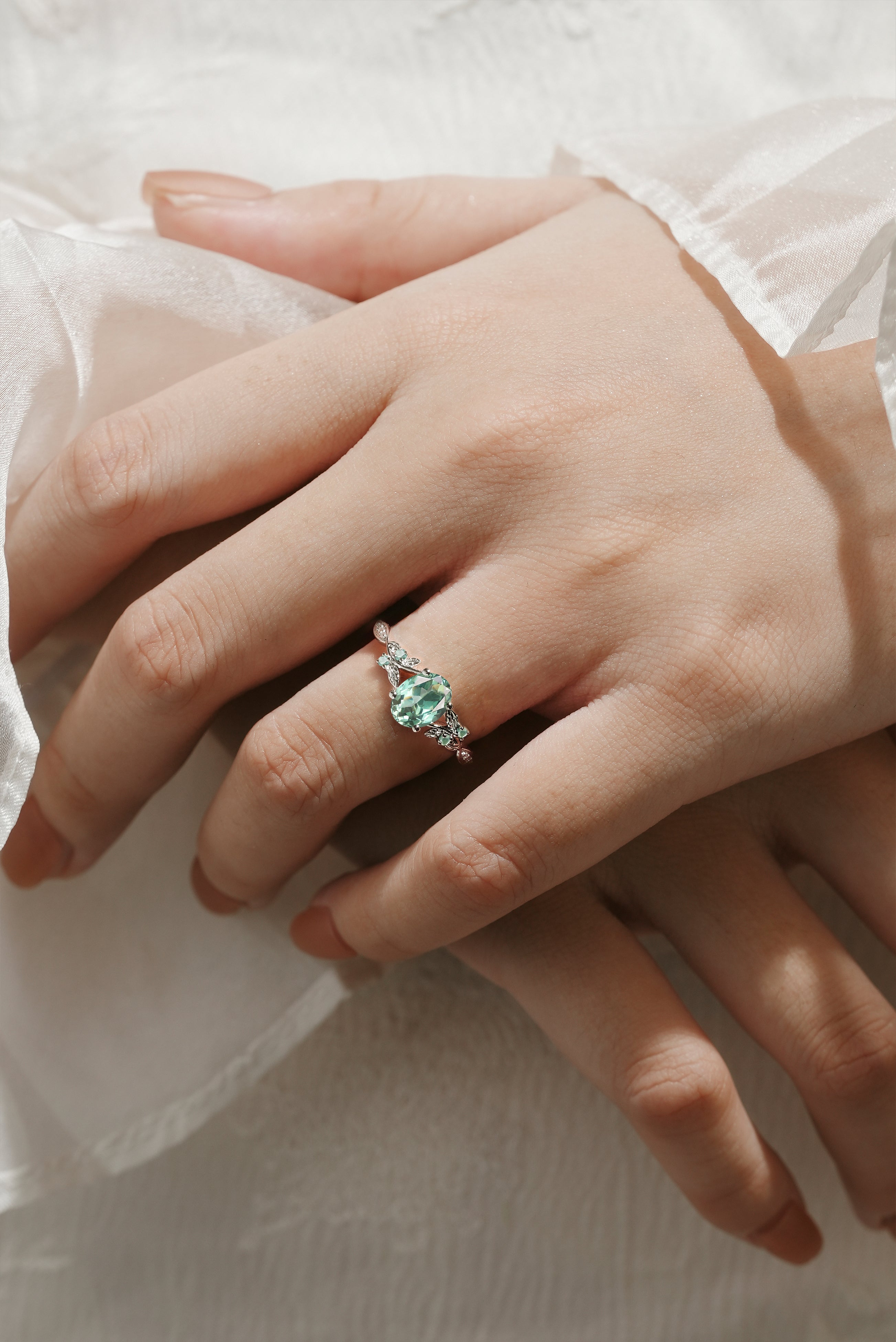Green sapphire engagement ring on hand with leaf design