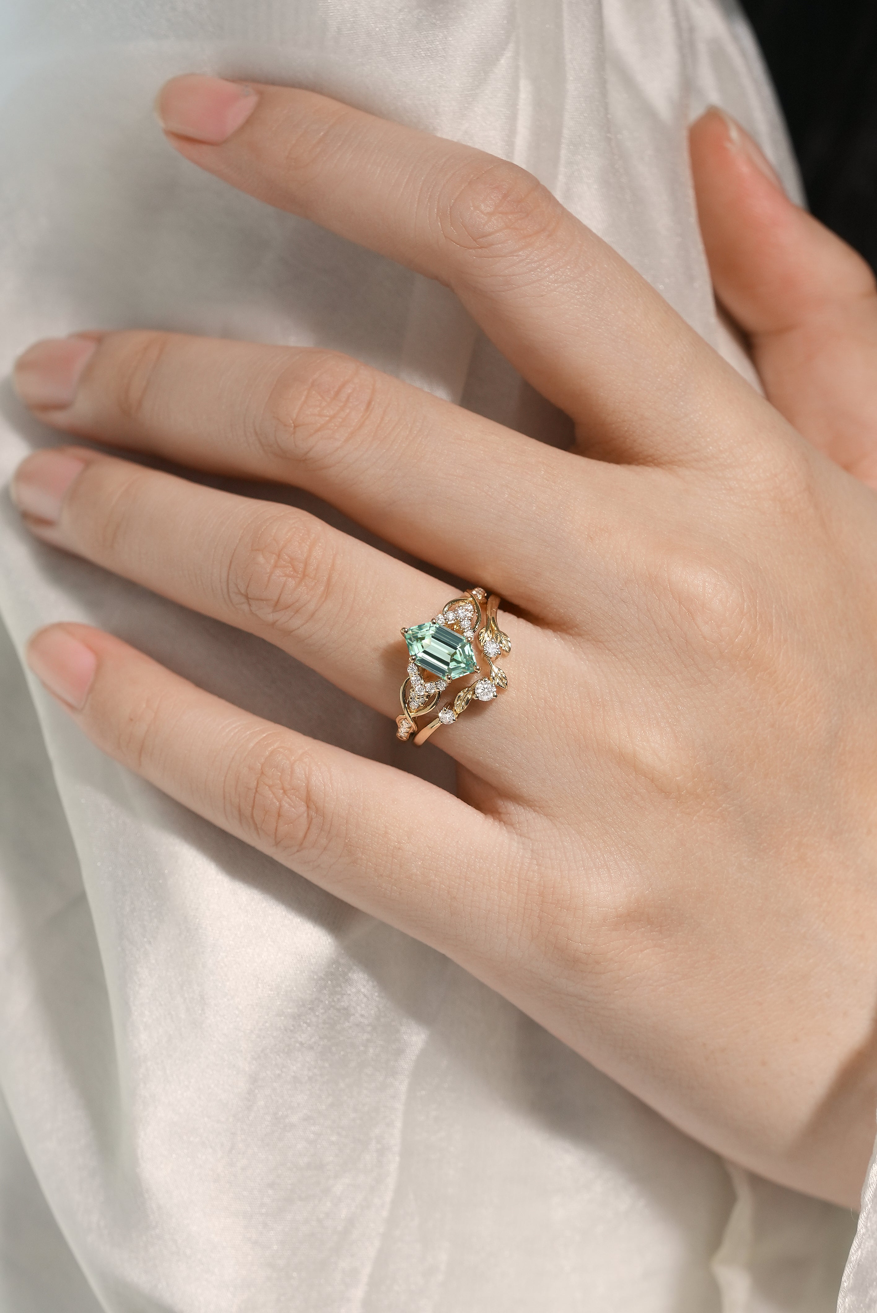 Woman's hand wearing green sapphire engagement ring and leaf wedding band