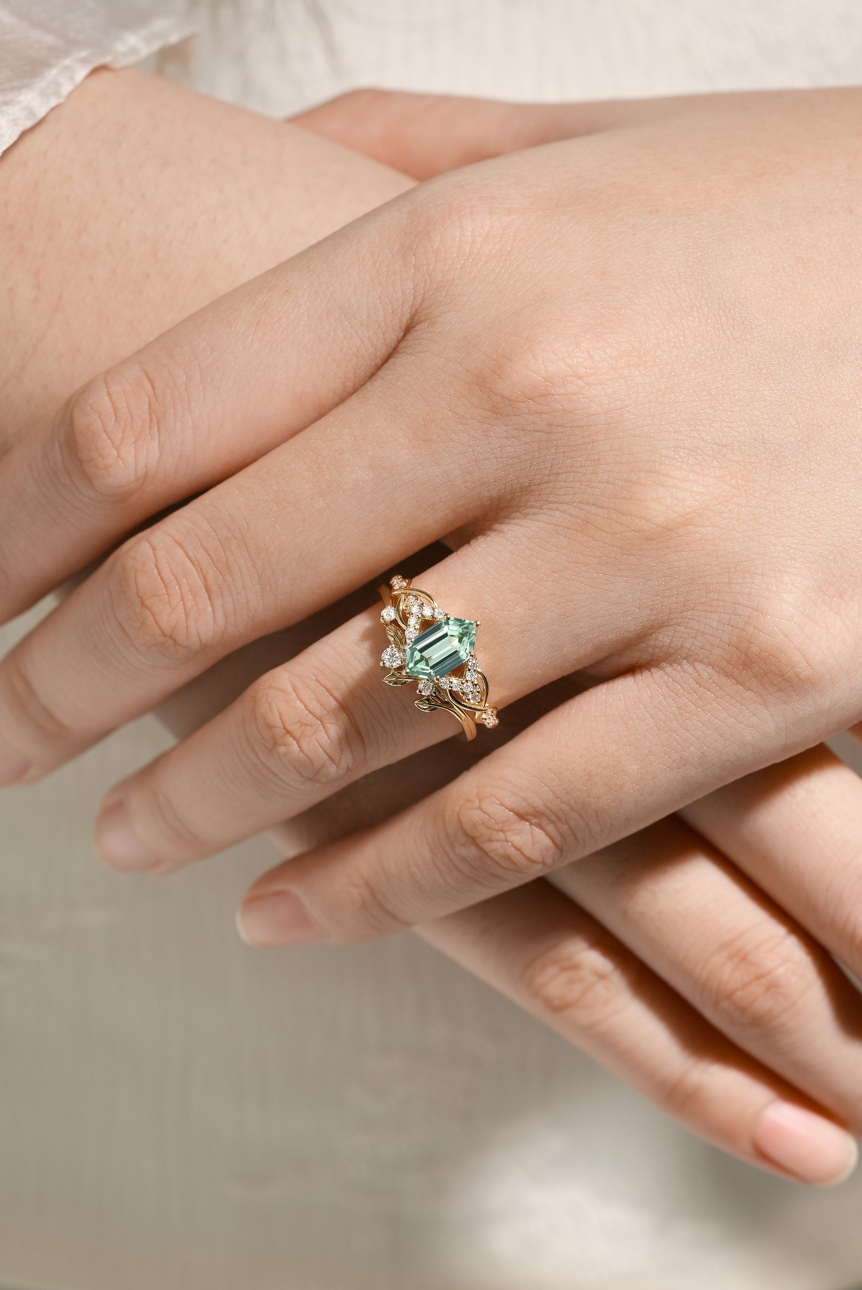 Close-up of a hand wearing nature-inspired green sapphire engagement ring and leaf wedding band