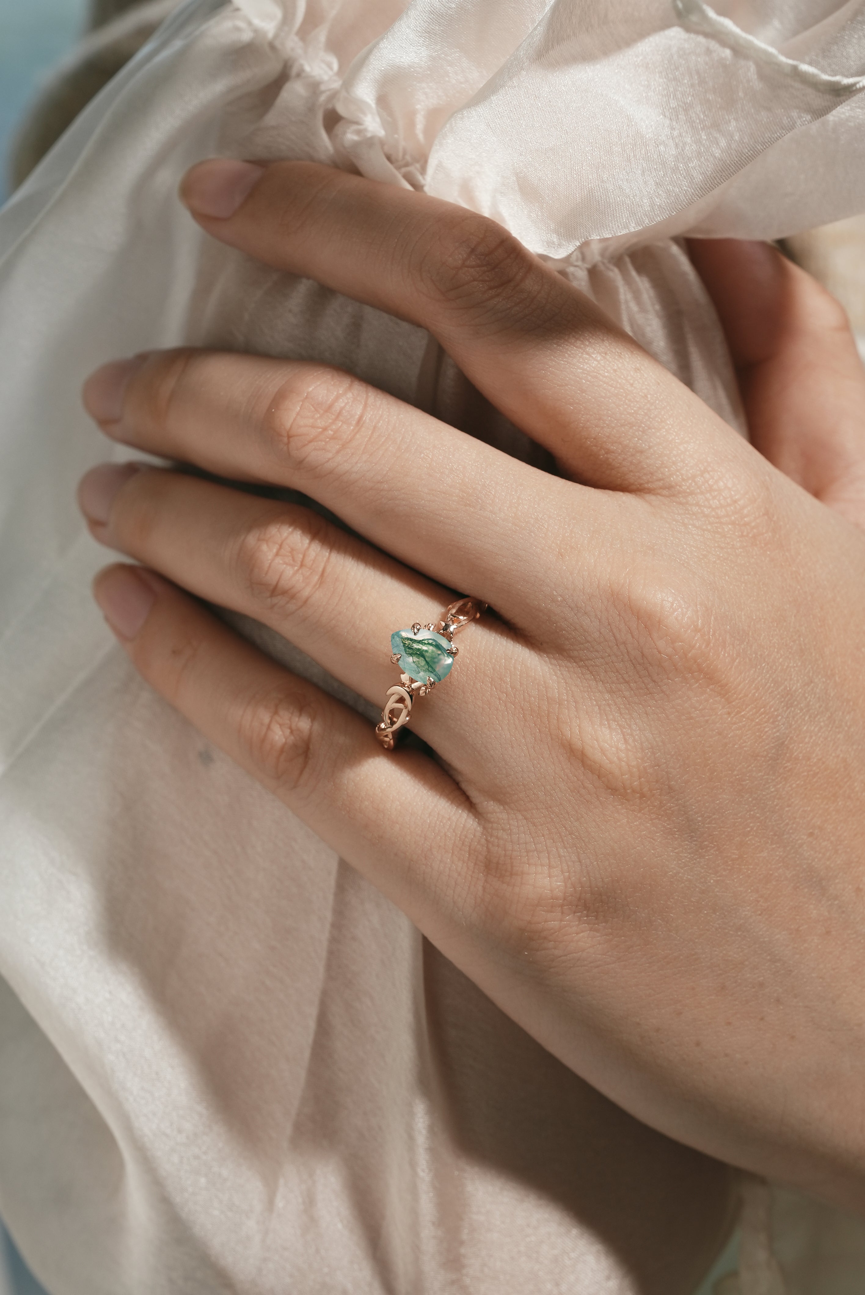 Woman's hand wearing pear cut moss agate engagement ring