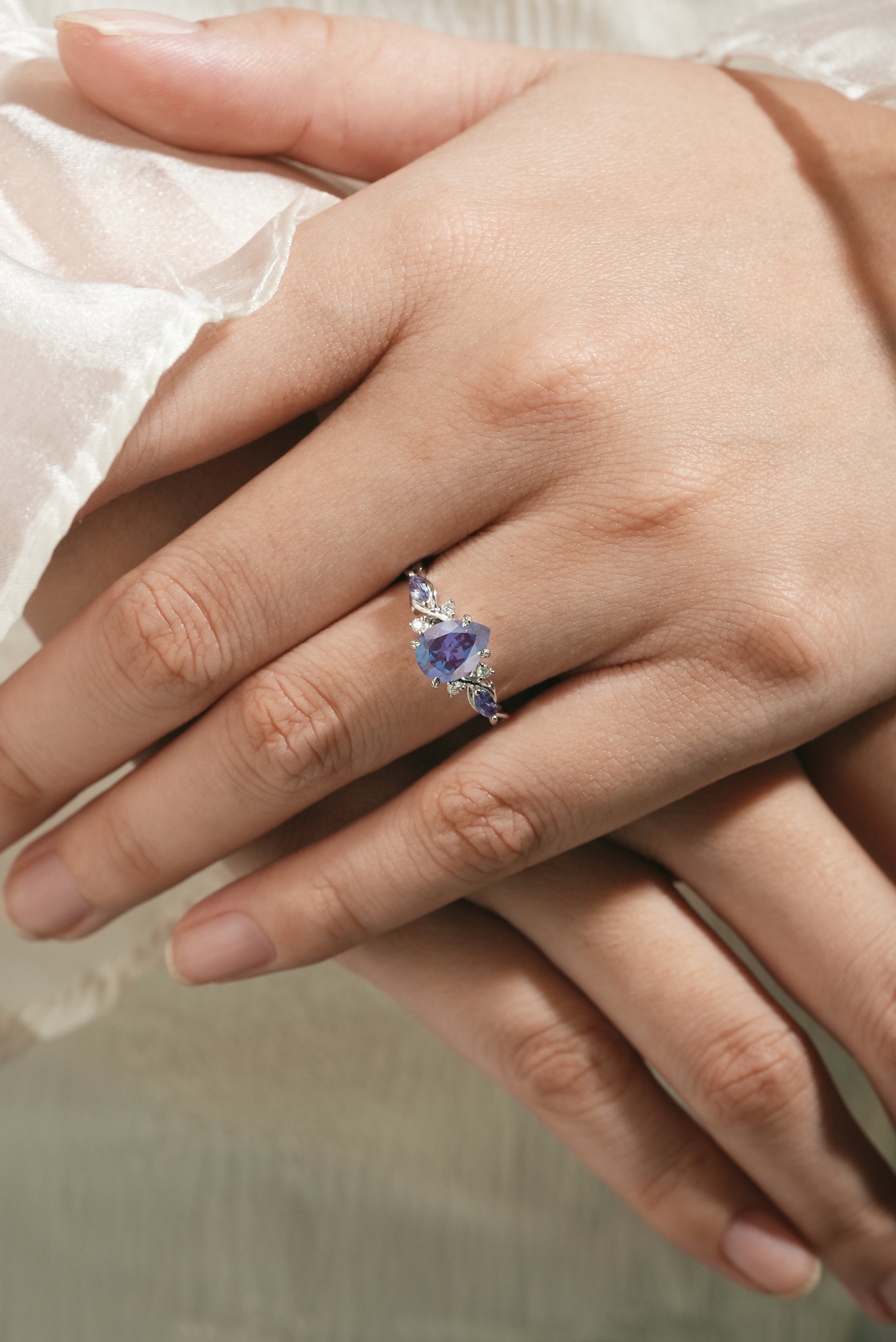 Elegant alexandrite engagement ring with pear-cut center stone on a hand, featuring moissanite accents. Lahela Jewelry.